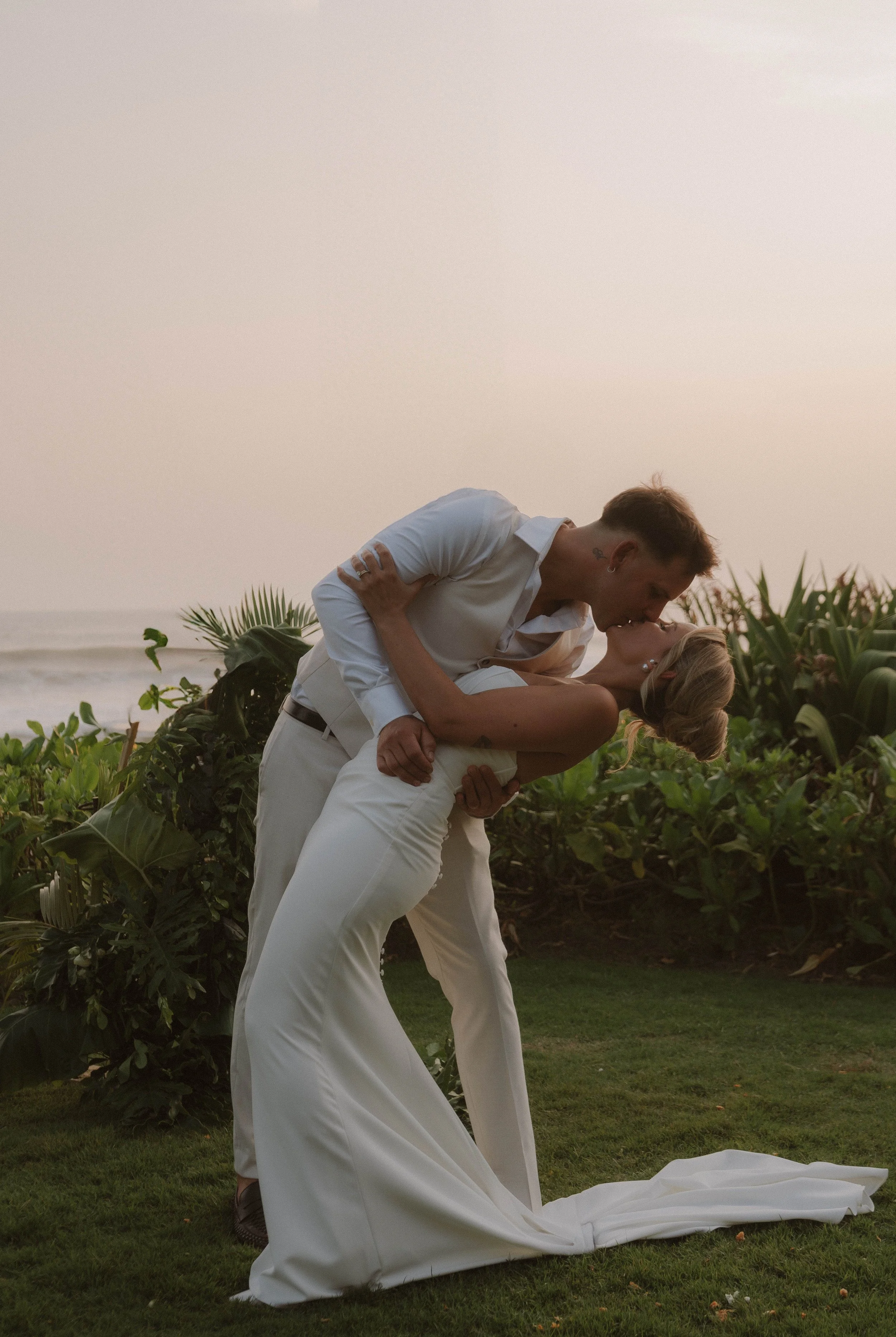 A couple kissing on a beach during sunset, with the man wearing a white shirt and light pants, and the woman in a white dress. yarra valley and Melbourne wedding photographer