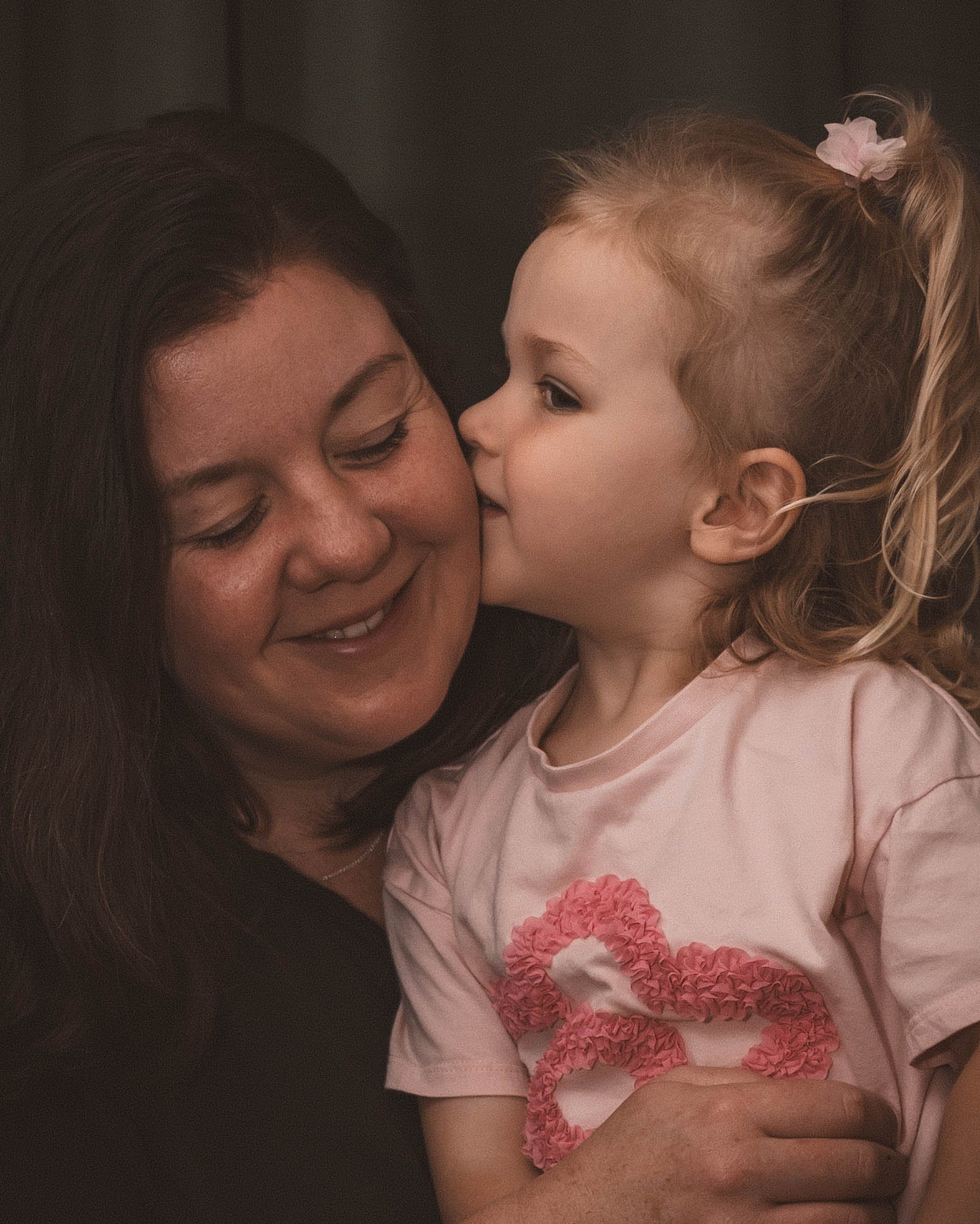 A woman smiling as a young girl gives her a kiss on the cheek.