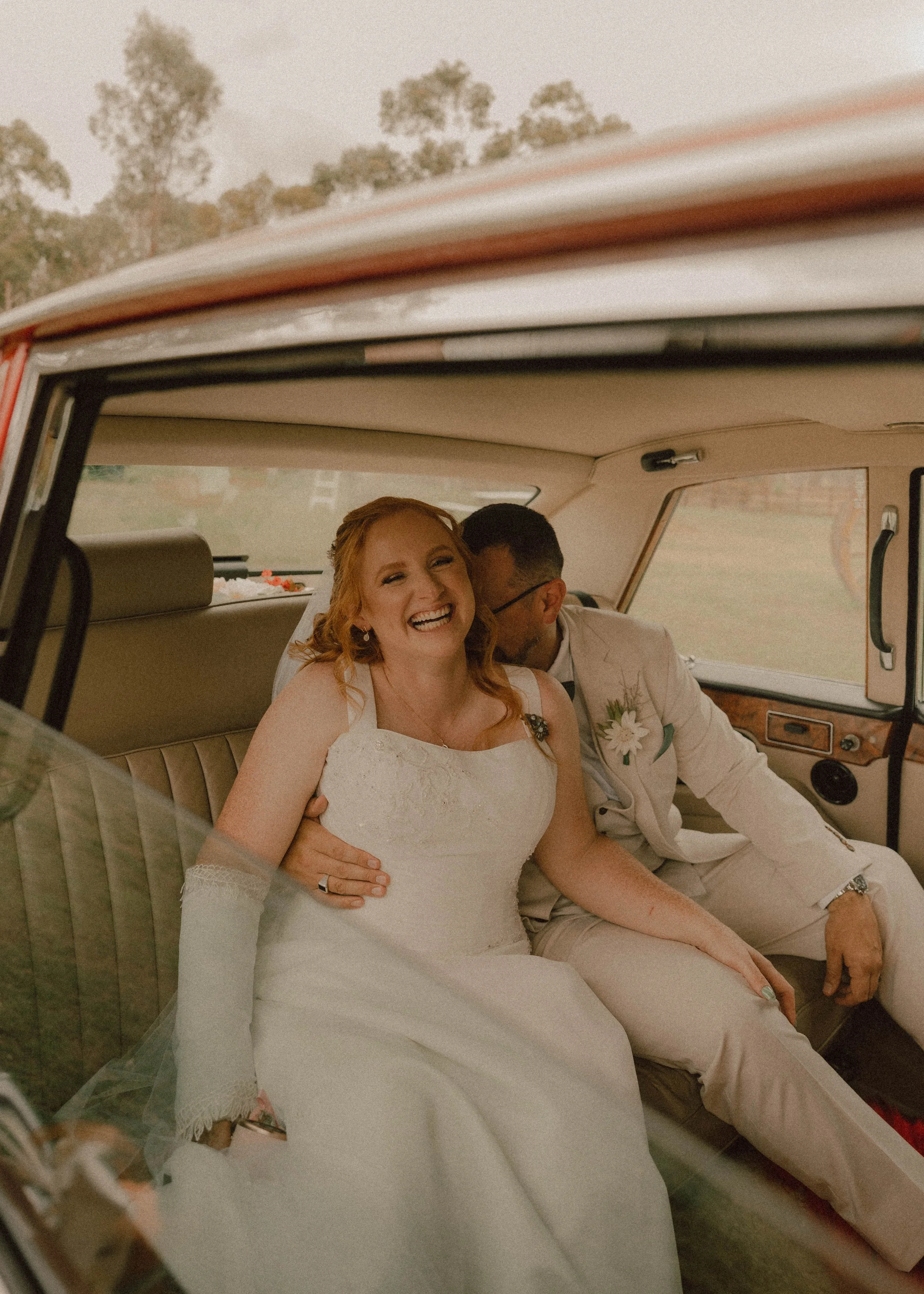 A bride and groom sitting inside a vintage car, smiling and enjoying their wedding day in Perth
