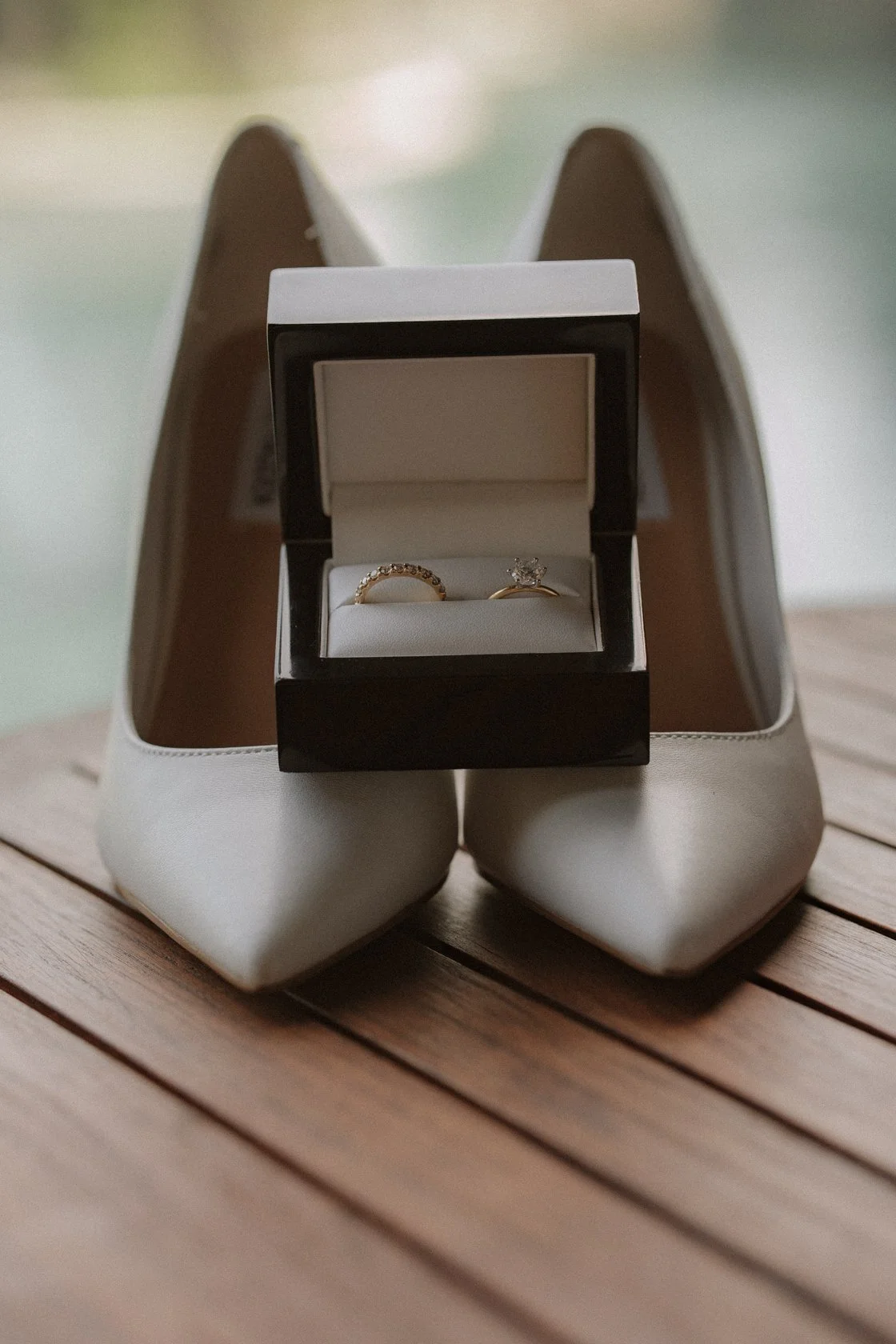A pair of white high-heeled shoes with a black ring box containing an engagement ring and a wedding band placed on top of them. yarra valley and Melbourne wedding photographer