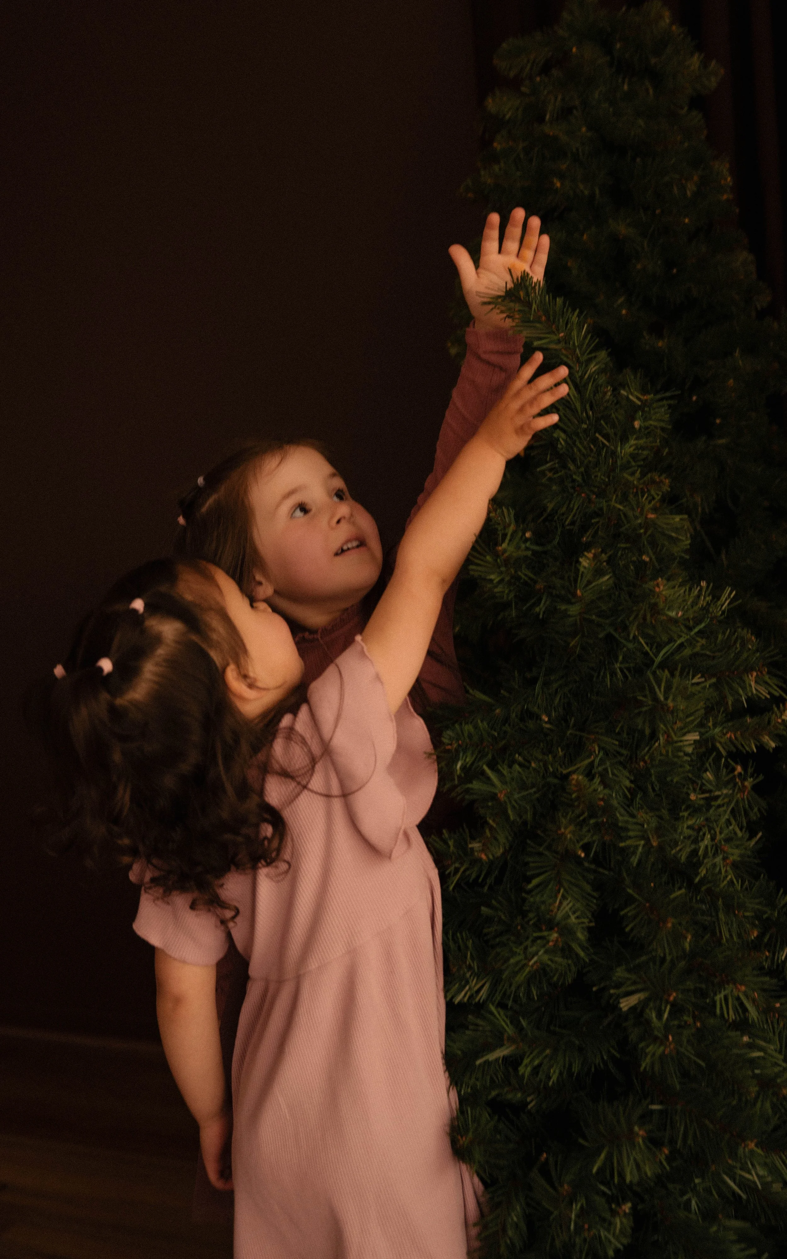 Children decorating a Christmas tree, with one girl reaching up to place an ornament. for their Christmas mini session photos