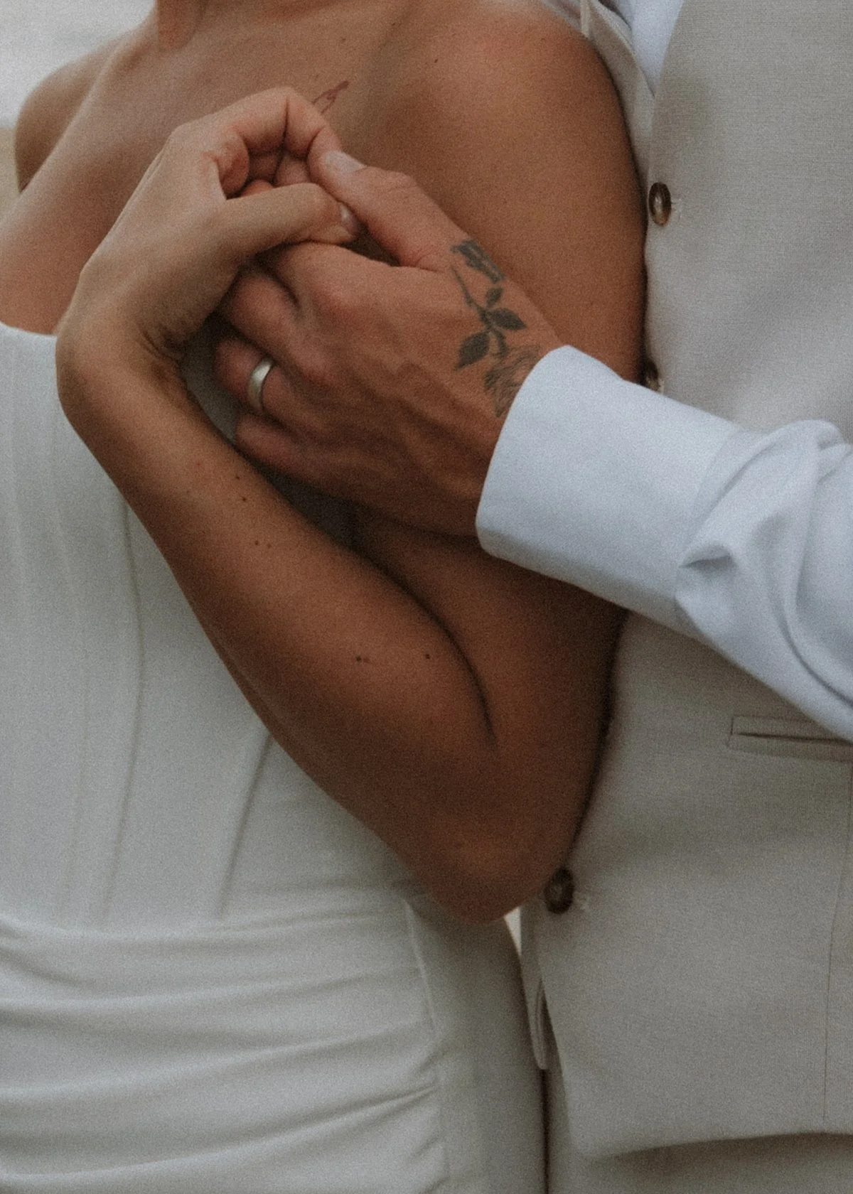 Two people holding hands, one person wearing a white shirt, the other person with a tattoo on their wrist, both seated on a white surface. yarra valley and Melbourne wedding photographer