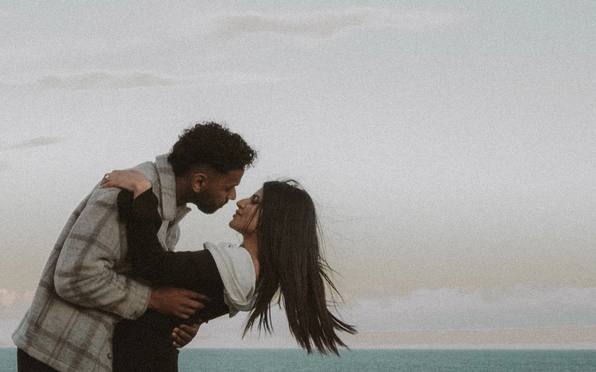 A couple sharing a passionate kiss on the beach at sunset, with ocean and cloudy sky in the background. moments after their proposal/engagement with jess a yarra valley and Melbourne wedding photographer