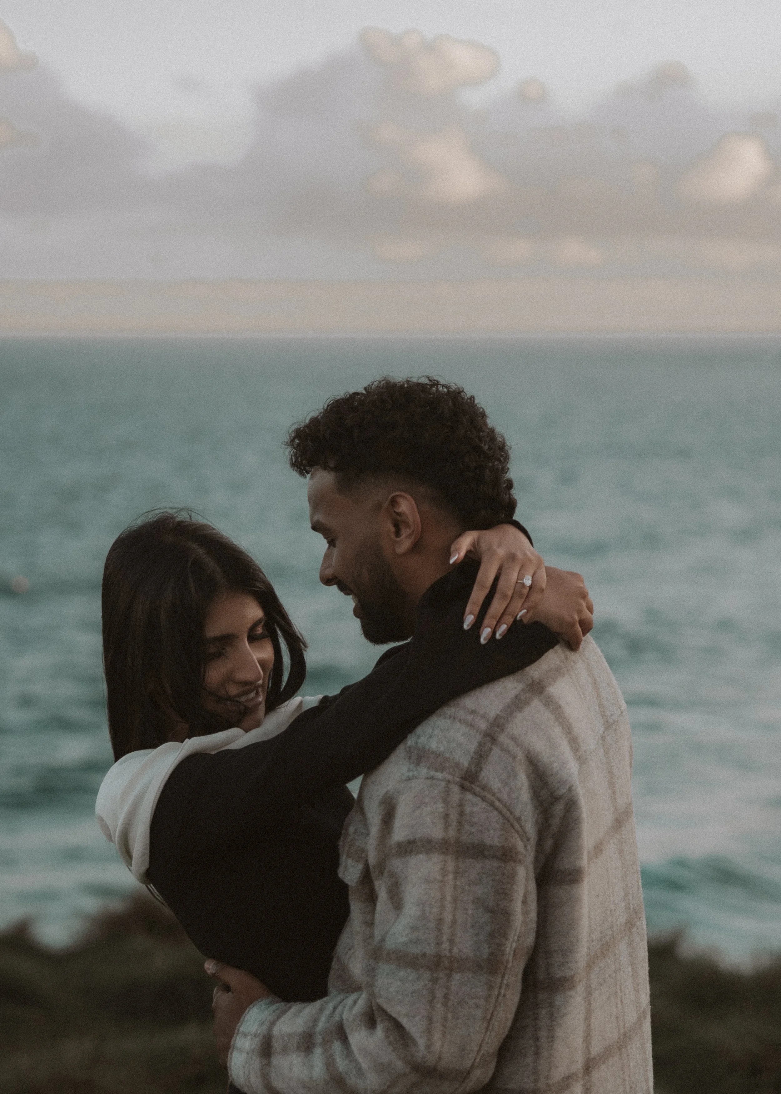 A couple embracing by the ocean with a cloudy sky in the background. moments after their engagement with jess a yarra valley and Melbourne wedding photographer