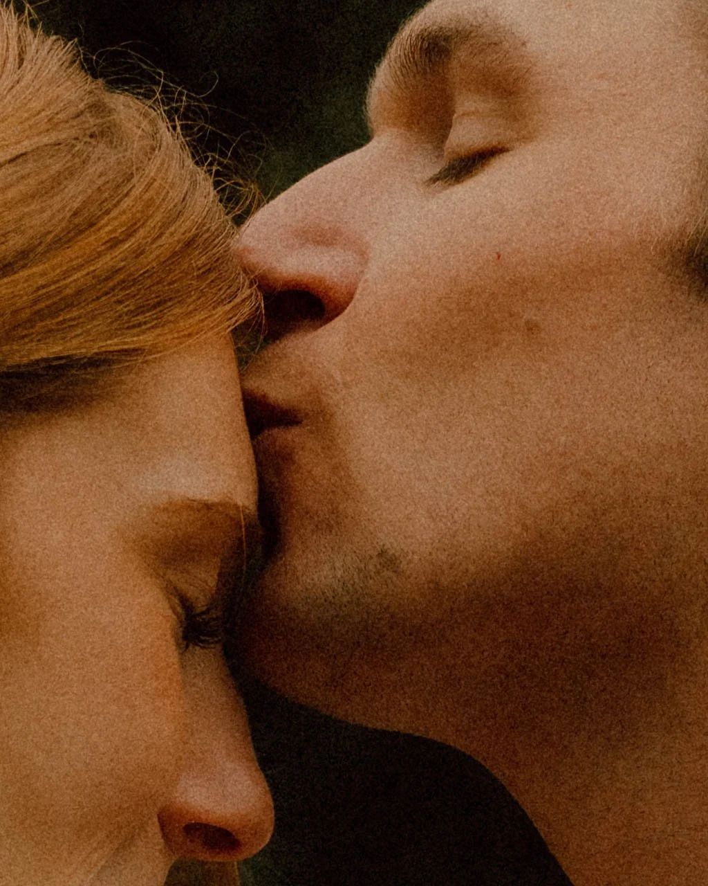 A close-up of a man kissing a woman on the forehead with their eyes closed.