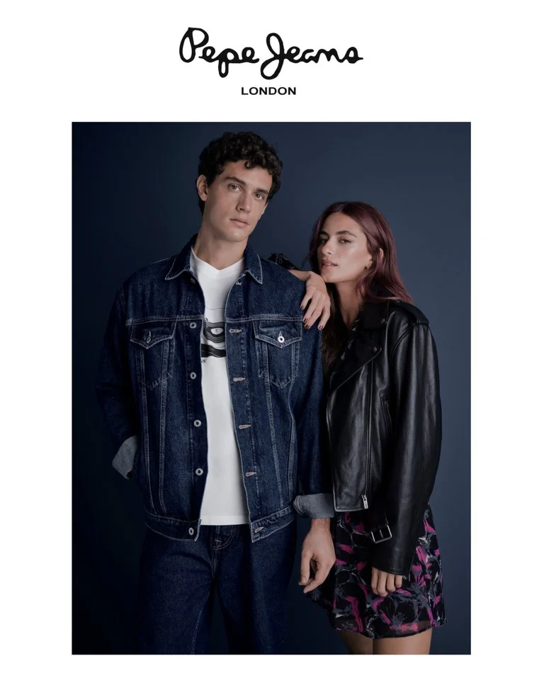 Two young adults, a man and a woman, posing together against a dark blue background. The man is wearing a denim jacket and jeans, and the woman is dressed in a black leather jacket and a patterned skirt. The text above them reads "Pepe Jeans London."