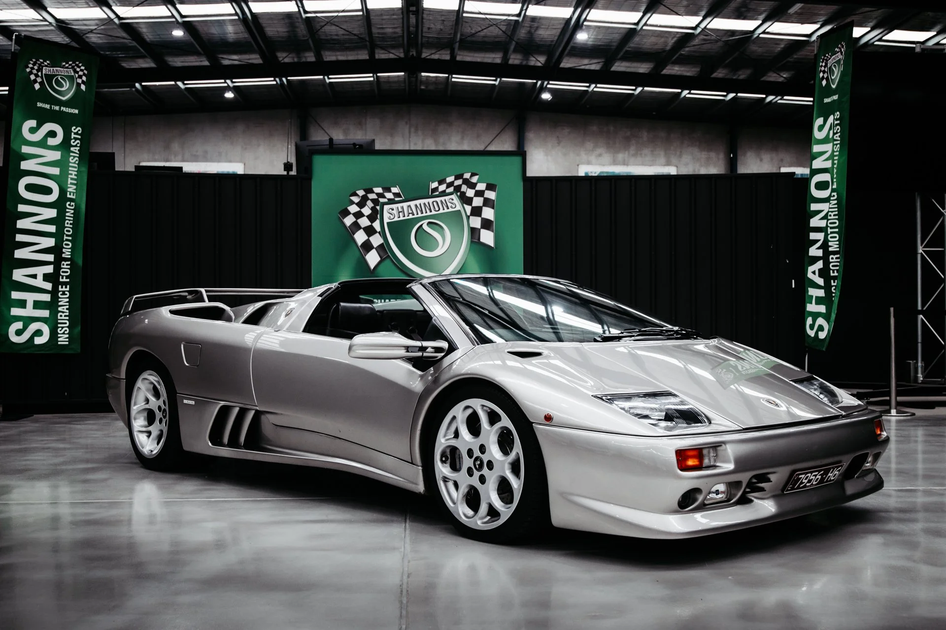 Silver Lamborghini Diablo sports car displayed indoors at an automotive event, with green banners reading 'Shannons' and 'Share the Passion' in the background.