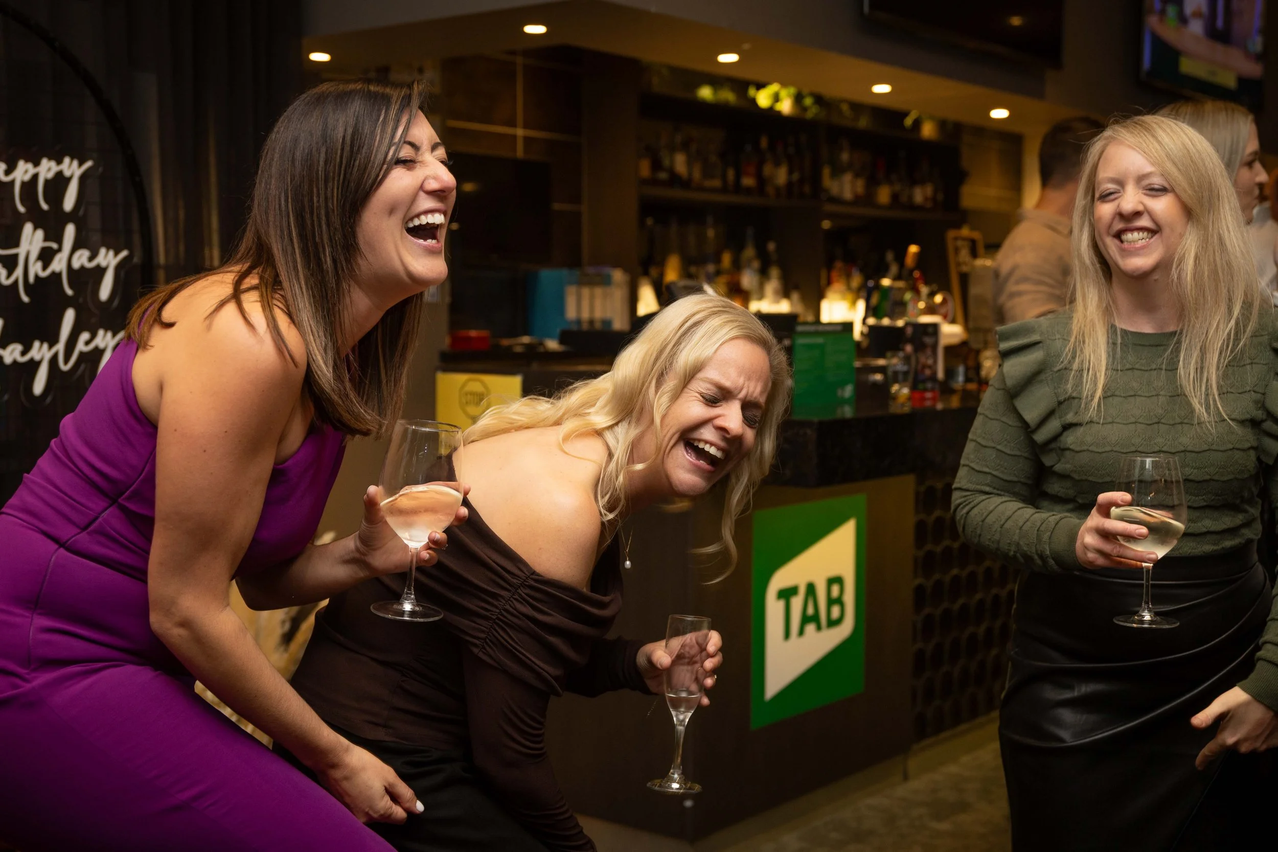 A colour image of three girls laughing at a 40th birthday party