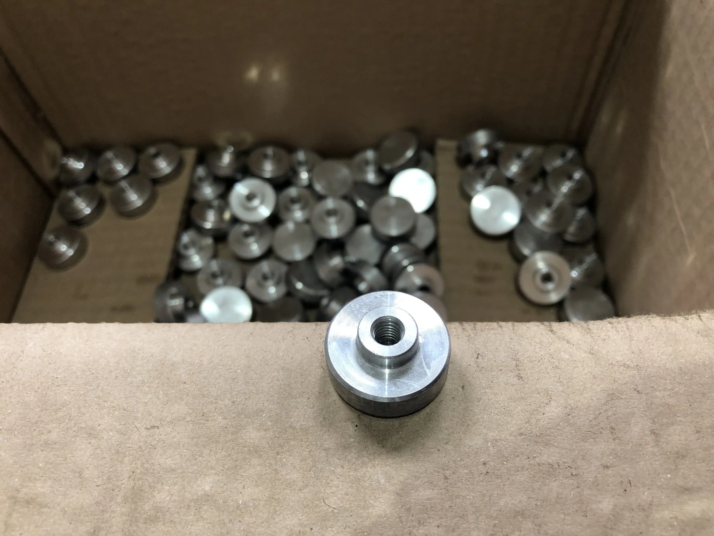 Set di piccole parti metalliche cilindriche in una scatola di cartone, con una parte metallica frontale in primo piano.