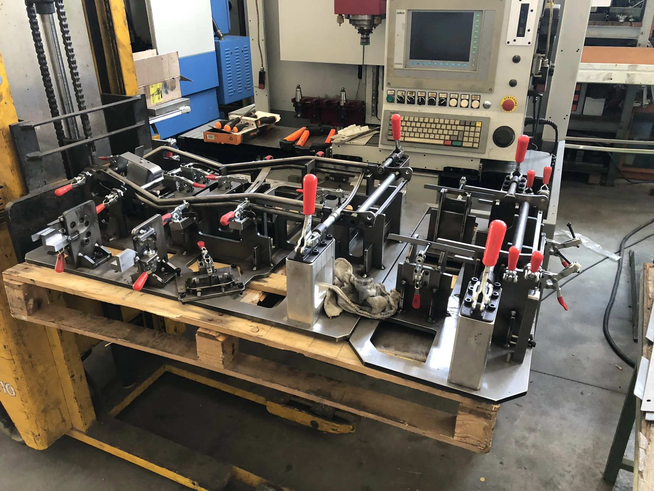 Particolare di un'attrezzatura industriale con alcune viti, una chiave inglese e un panno su una base di metallo, in un'officina