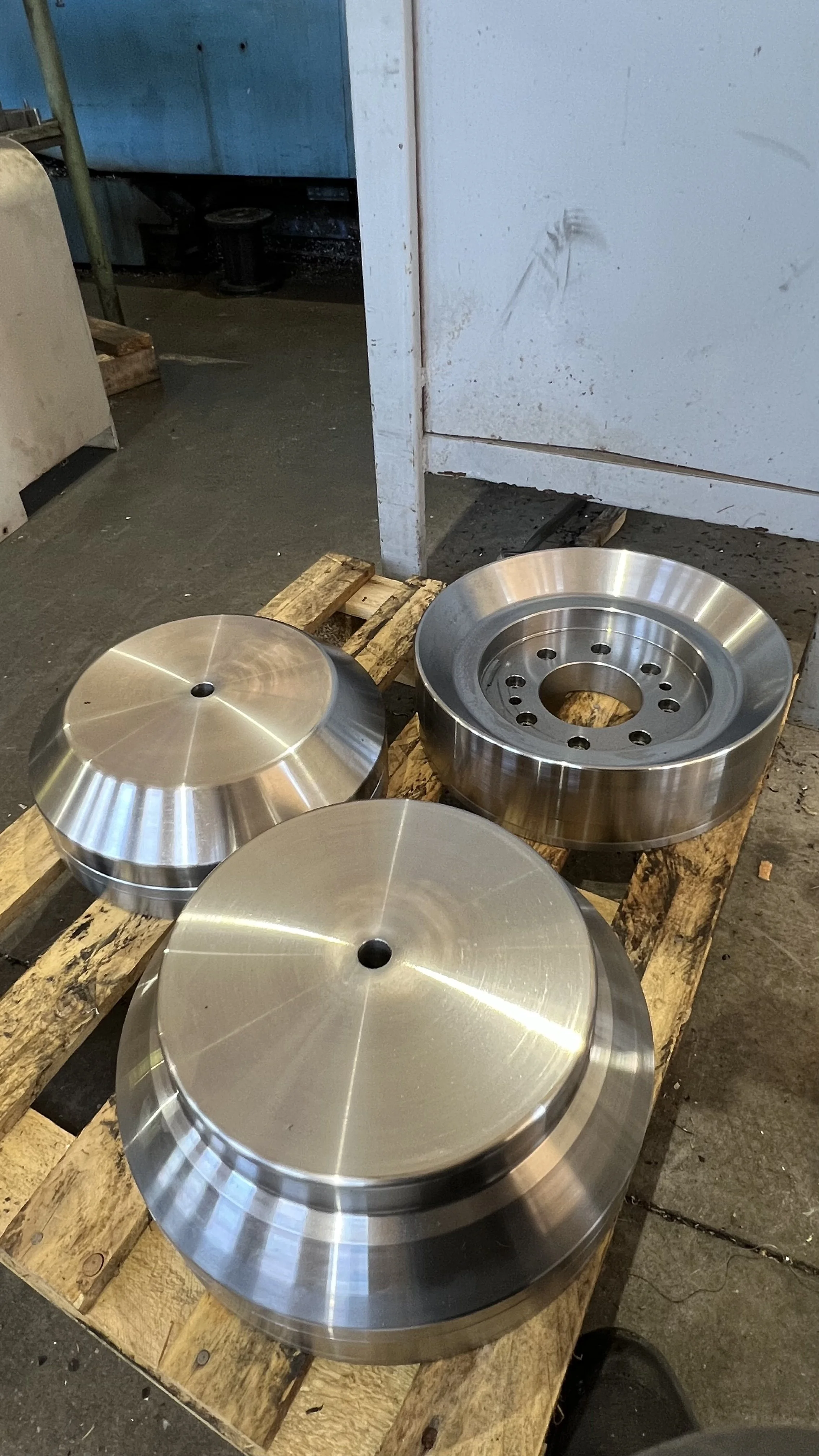 Tre ruote di metallo con superficie lucida, posizionate su un support di legno in un ambiente industriale.