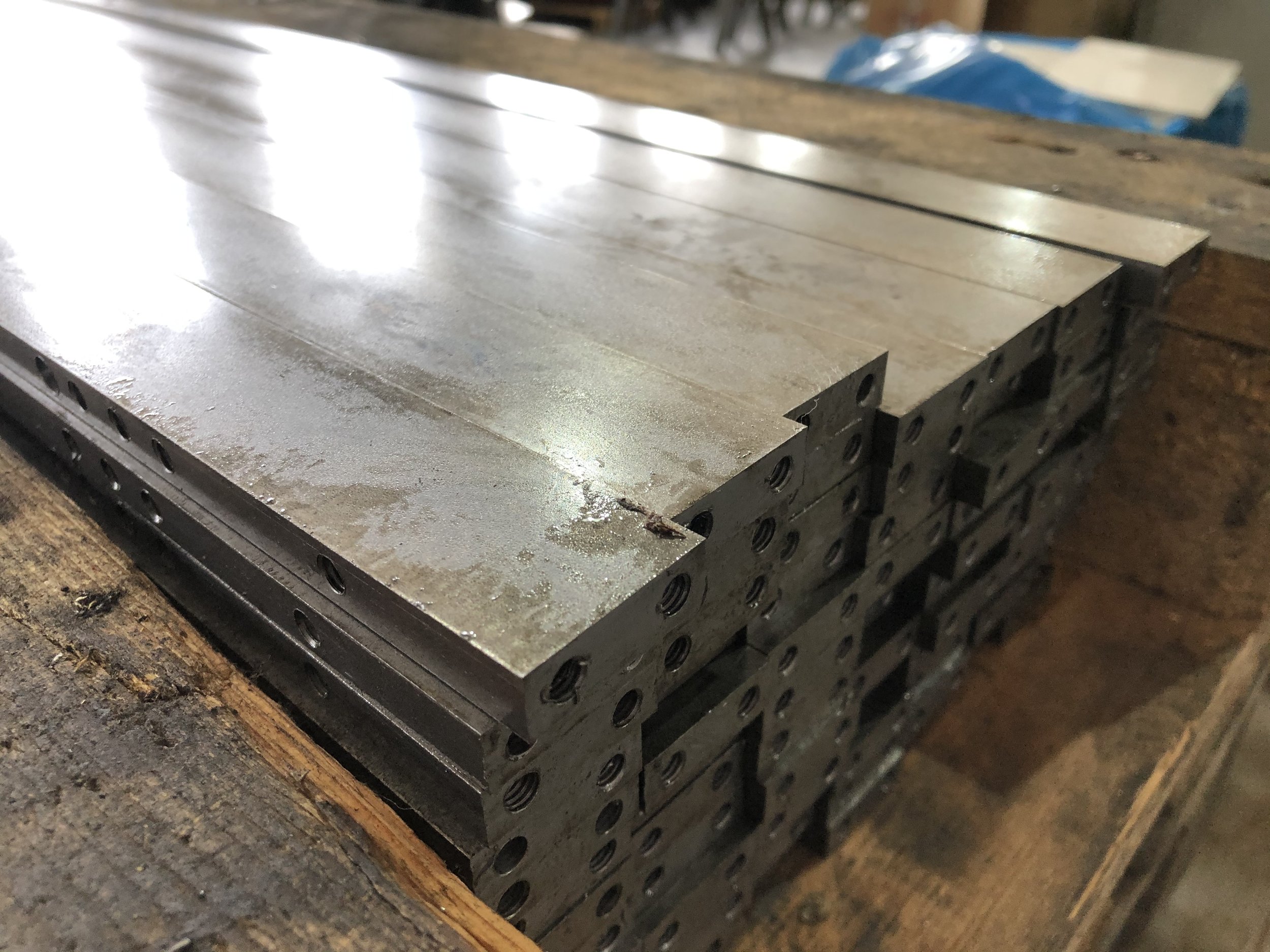 Finiture metalliche di pezzi di macchinario impilati su un banco di lavoro di legno.