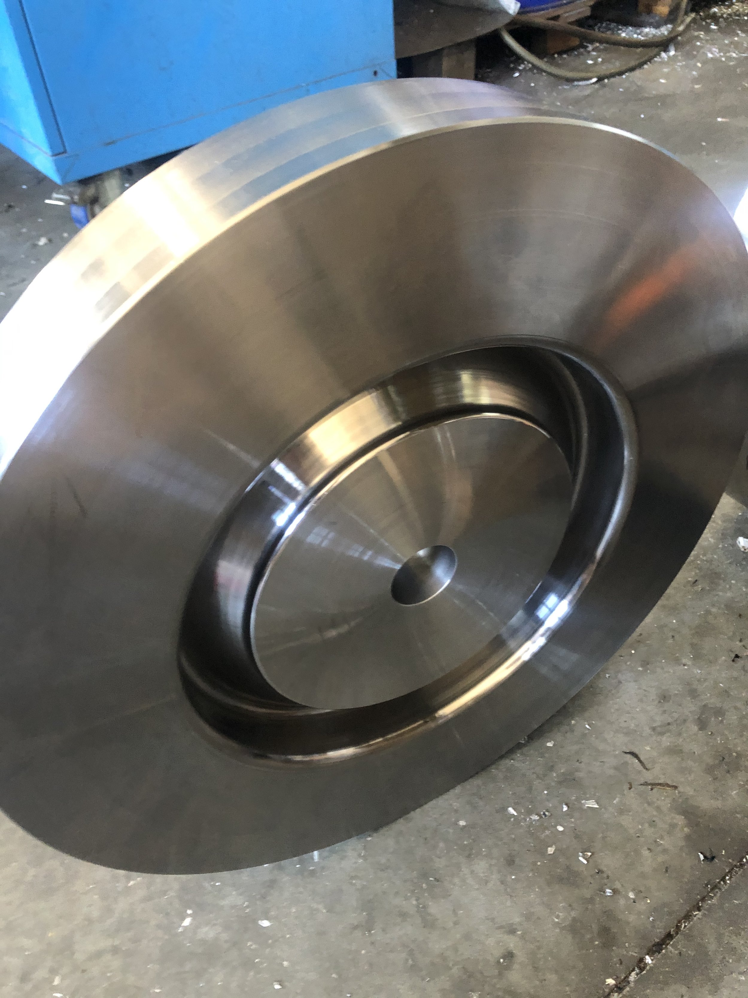 Una grande ruota di acciaio lucido con un cuscinetto al centro, poggiata su un pavimento in cemento.