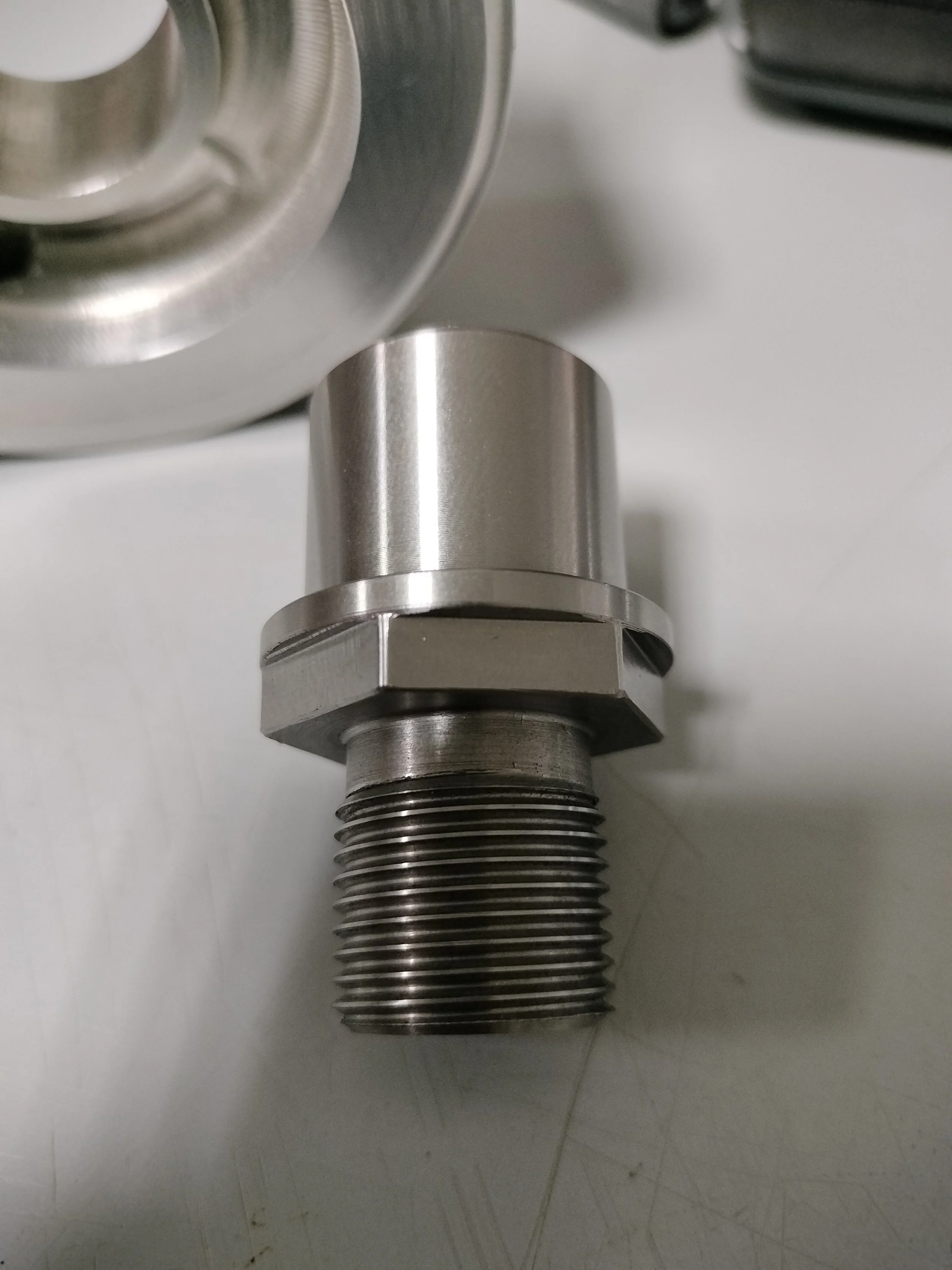 Particolare di una vite o bullone in metallo con filetto. Sospeso, con altre parti metalliche sullo sfondo.