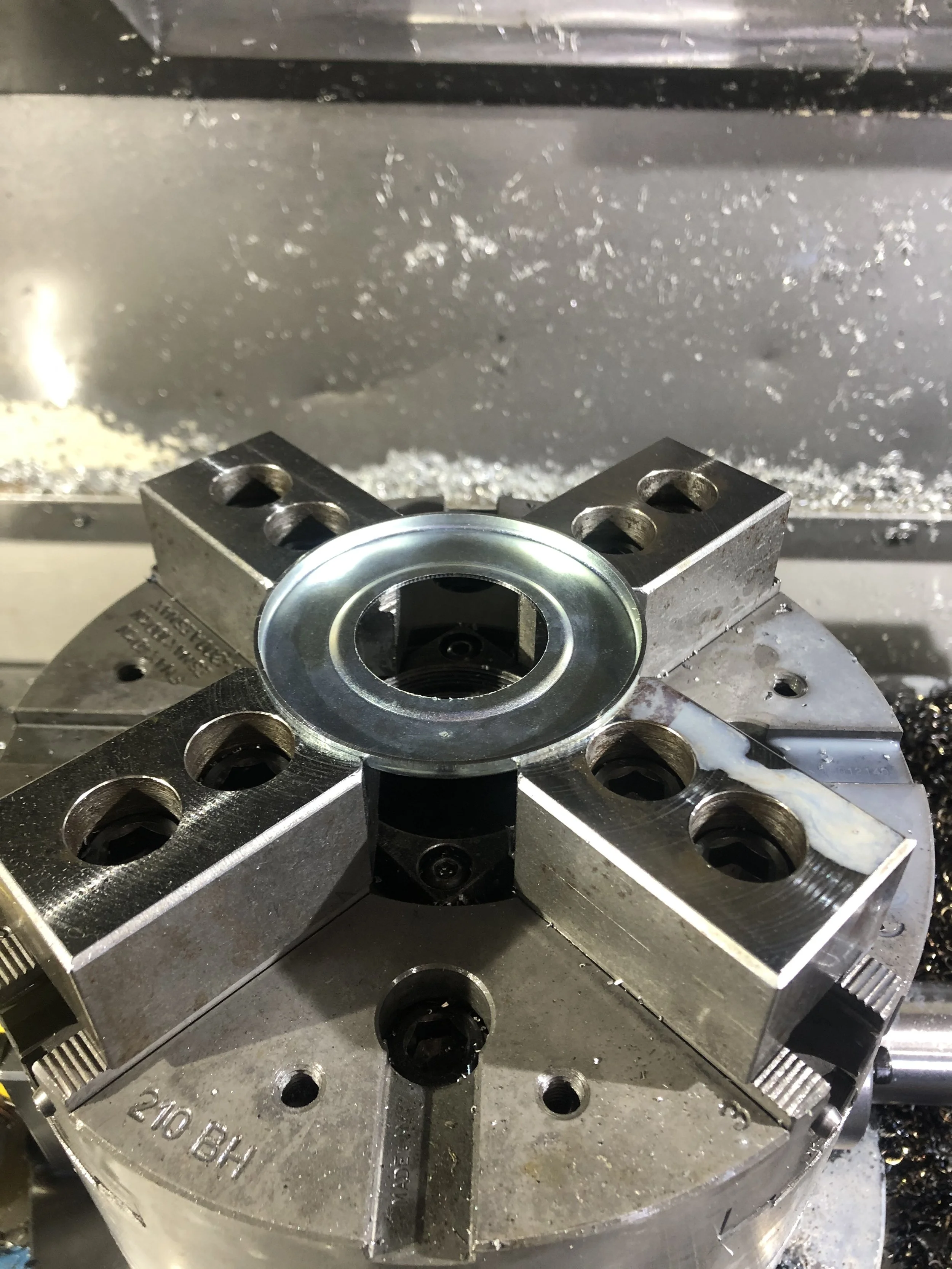 Particolare di una macchina utensile in azione con pezzi di metallo e trucioli di sfrido sul piano di lavoro.