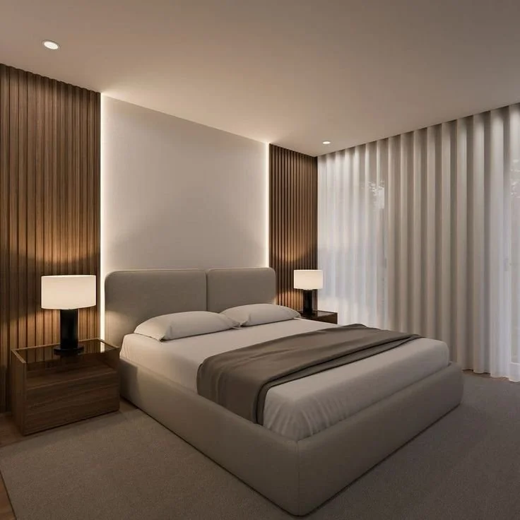 Modern bedroom with a large bed, neutral bedding, and two nightstands with lamps, beige curtain, and wooden wall panels.