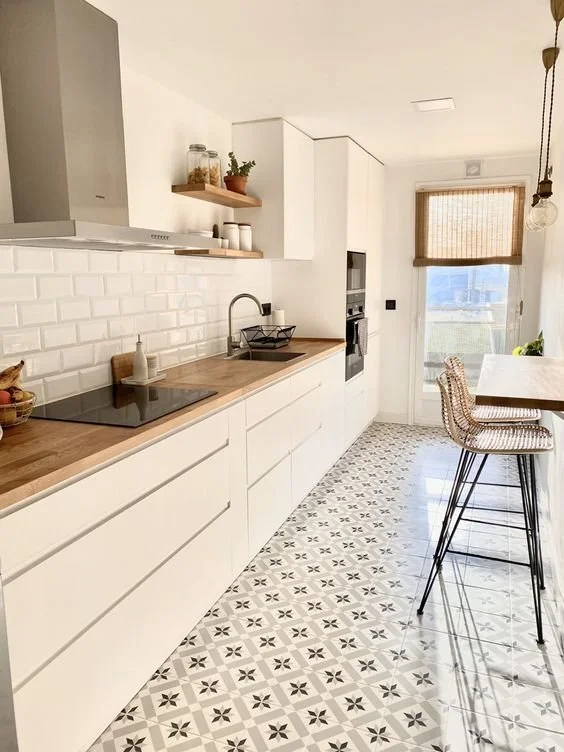 Modern white kitchen with patterned tile floor, wooden countertop, open shelving, built-in oven, and a window with a woven blind.