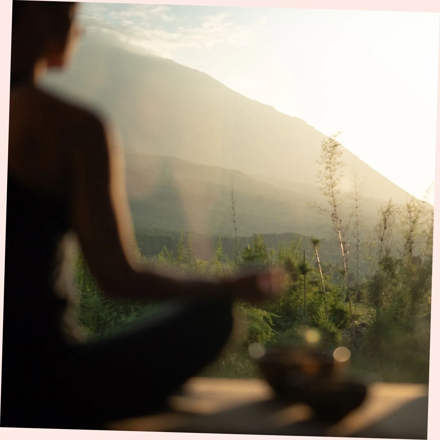 A person sitting in meditation with a mountain and trees in the background during sunset.