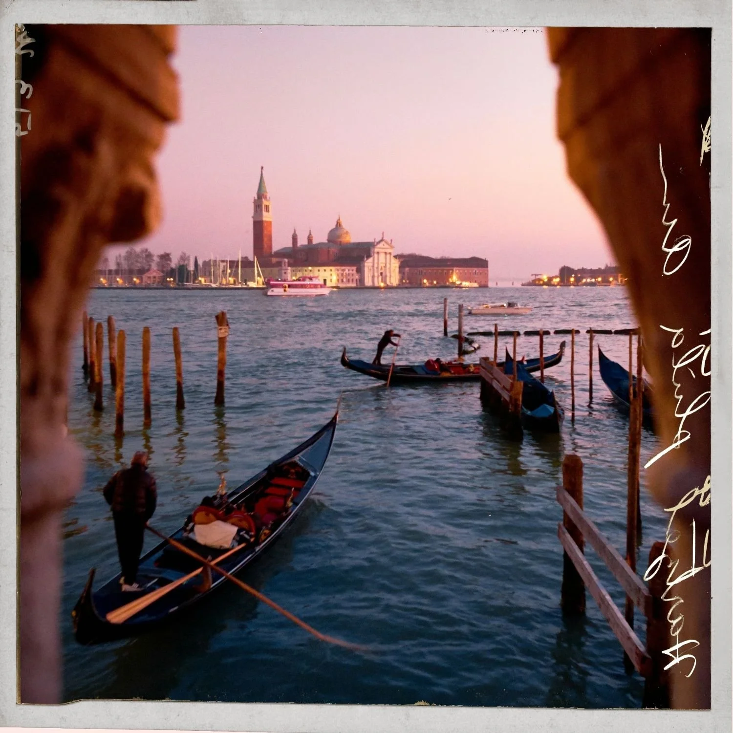 View of a Venice canal at sunset with gondolas docked, the Basilica di San Giorgio Maggiore in the background, and a pinkish sky.