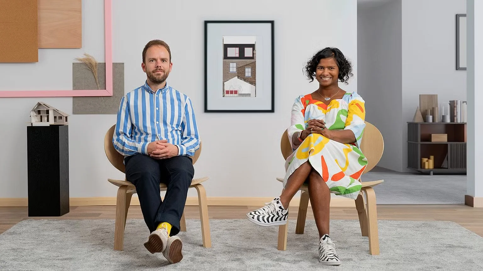 Black and white portrait of a young woman with curly hair, wearing a plaid long-sleeve shirt and earrings, smiling at the camera.