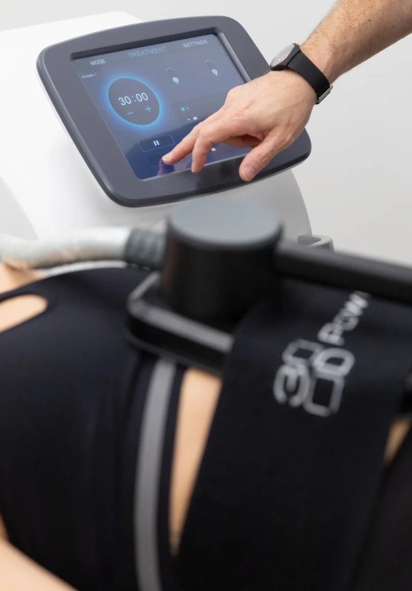 A person's hand operating a touchscreen control panel on a medical or rehabilitation device, with a focus on the screen displaying a timer and settings.