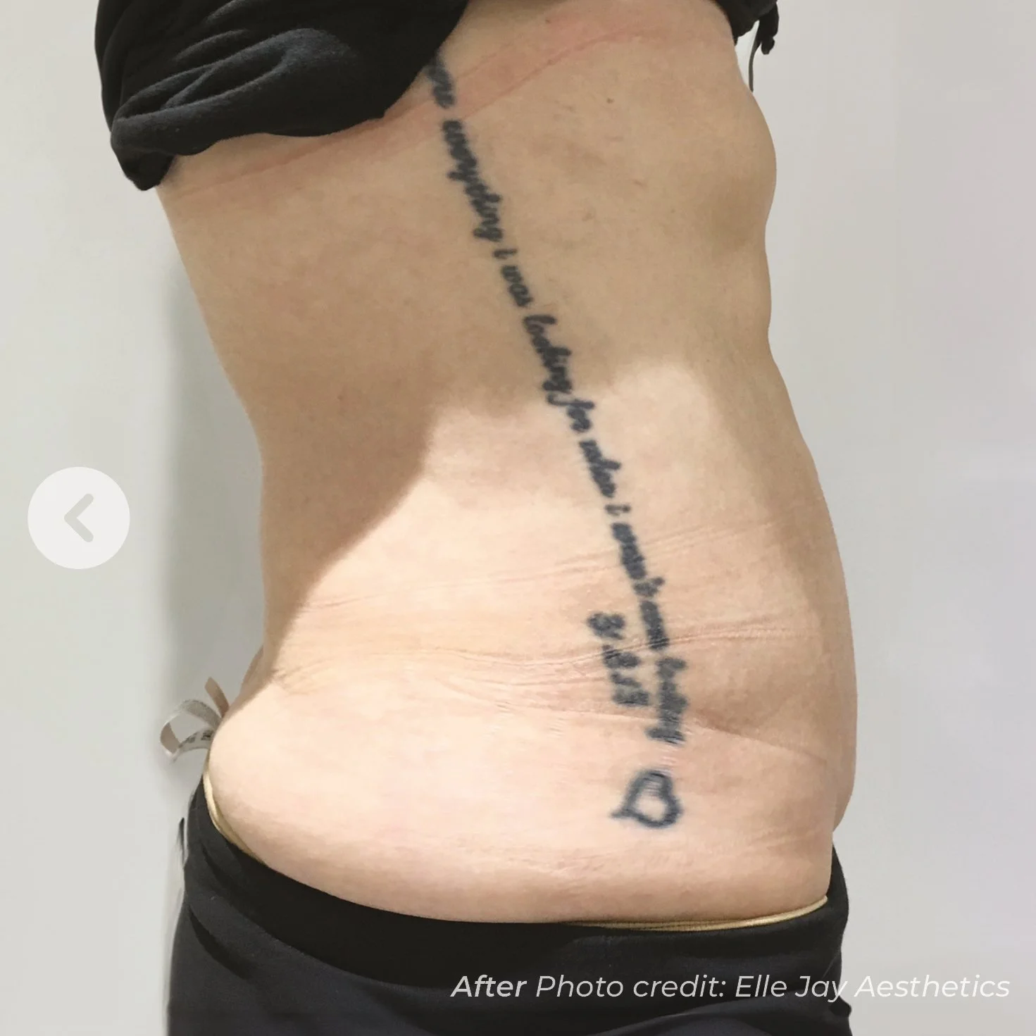 Side view of a man's abdomen and side, showing a large tattoo with cursive text running vertically along his side, wearing dark pants and a black shirt pulled up to reveal the tattoo.