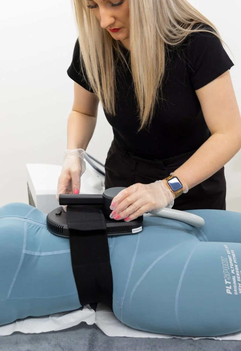 A medical technician performing a procedure on a patient lying on an examination table, using a device that appears to be for therapeutic or diagnostic purposes.