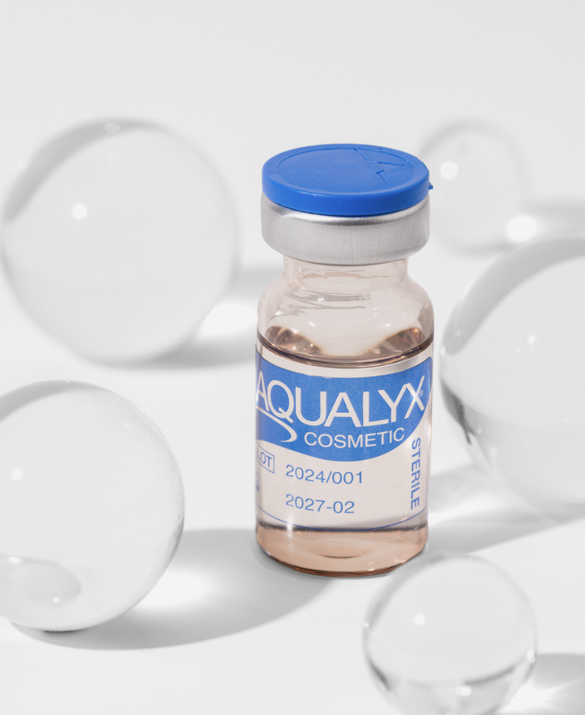 A small vial labeled 'Aqualyx Cosmetic' with a blue cap, surrounded by white spherical objects on a white background.