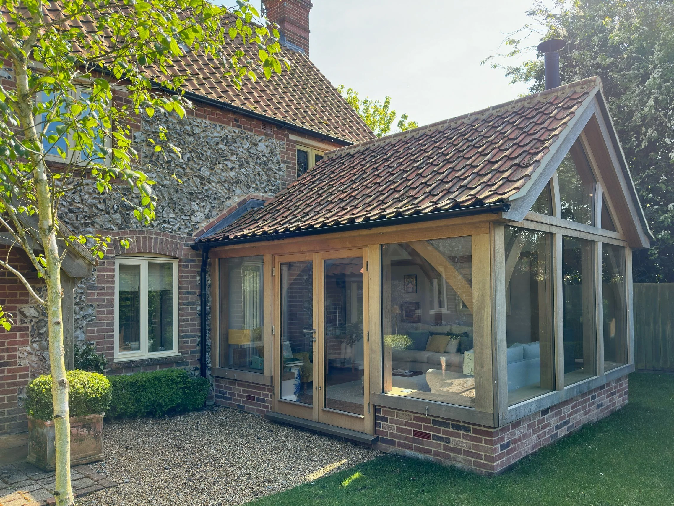 Oak frame garden room on a flint cottage with traditional pantile roof.