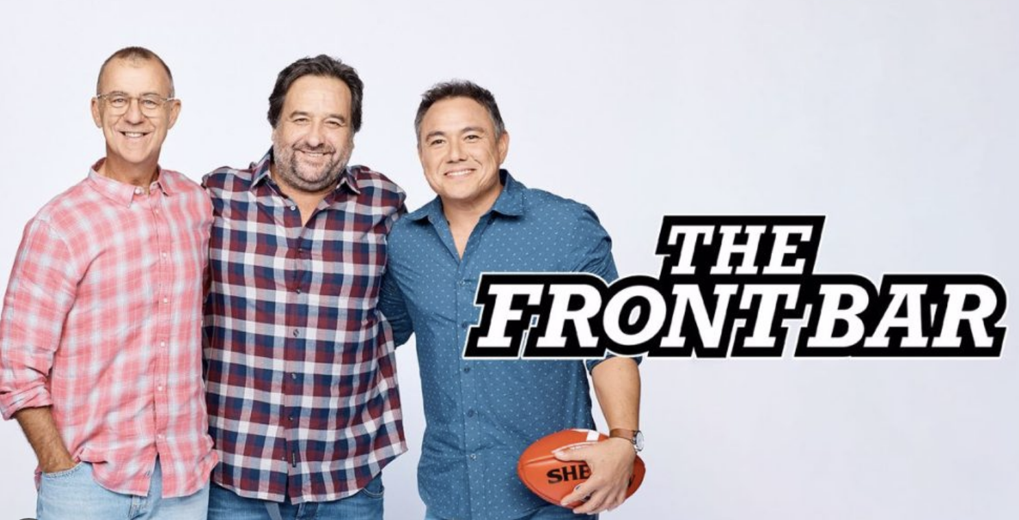 Three men standing together smiling, with a logo that reads 'The Front Bar' next to them, and one holding an Australian football.