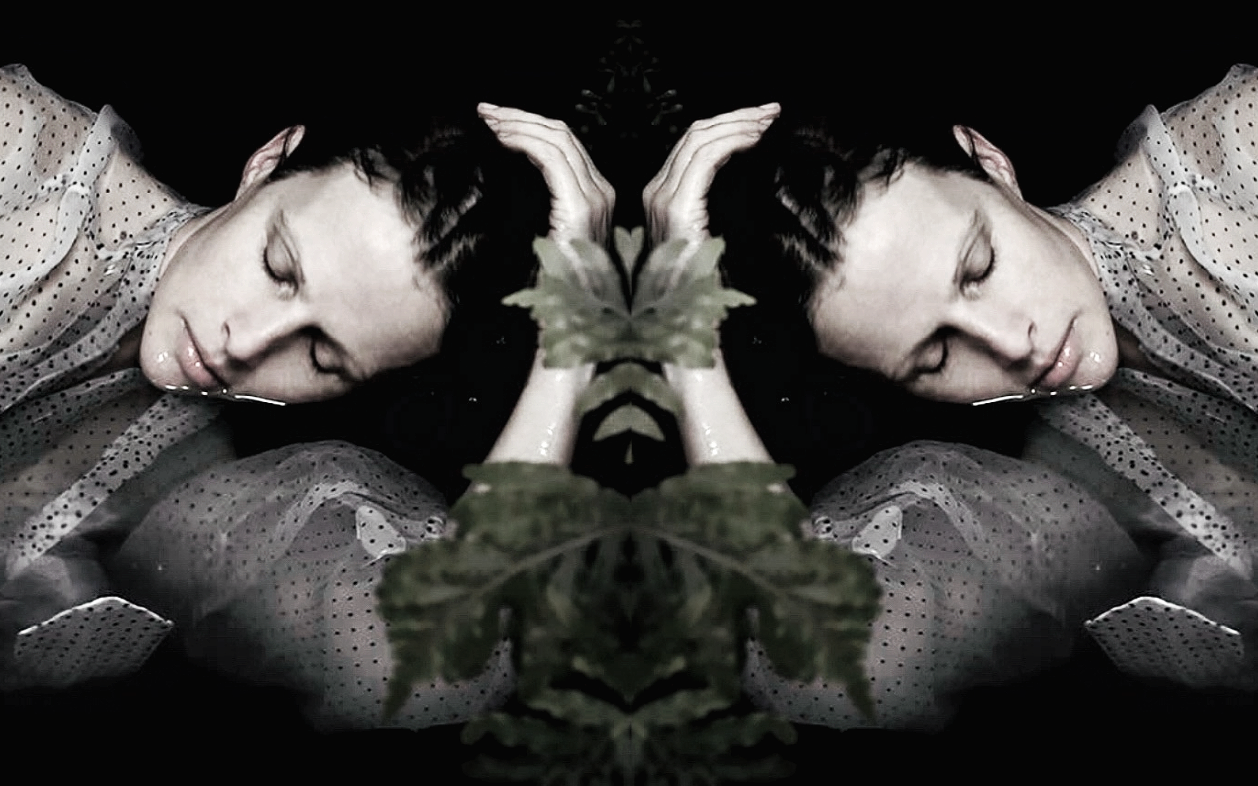 A mirrored image of a woman with short dark hair, eyes closed, leaning on a reflective black surface, with her hands behind her head and a green leafy plant in front.