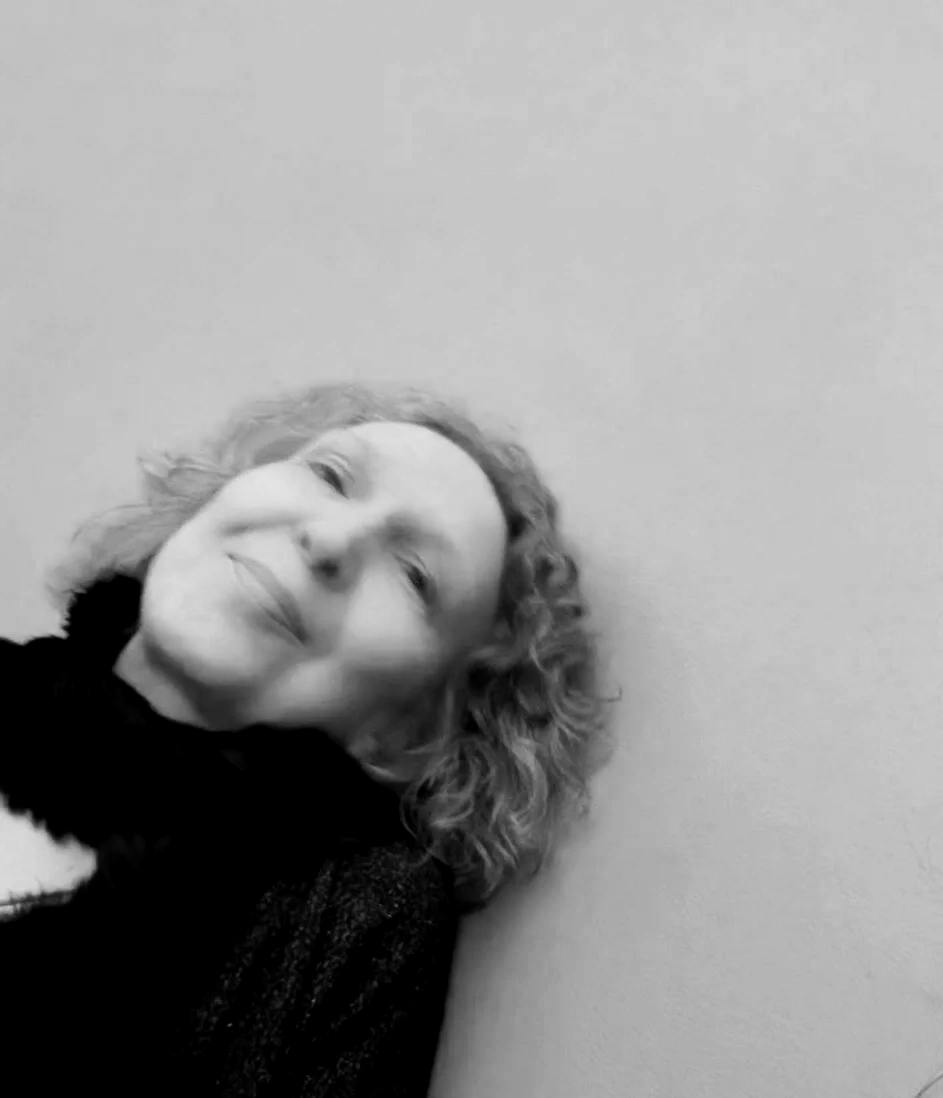 Black and white photo of a smiling woman with curly hair leaning her head against a wall.