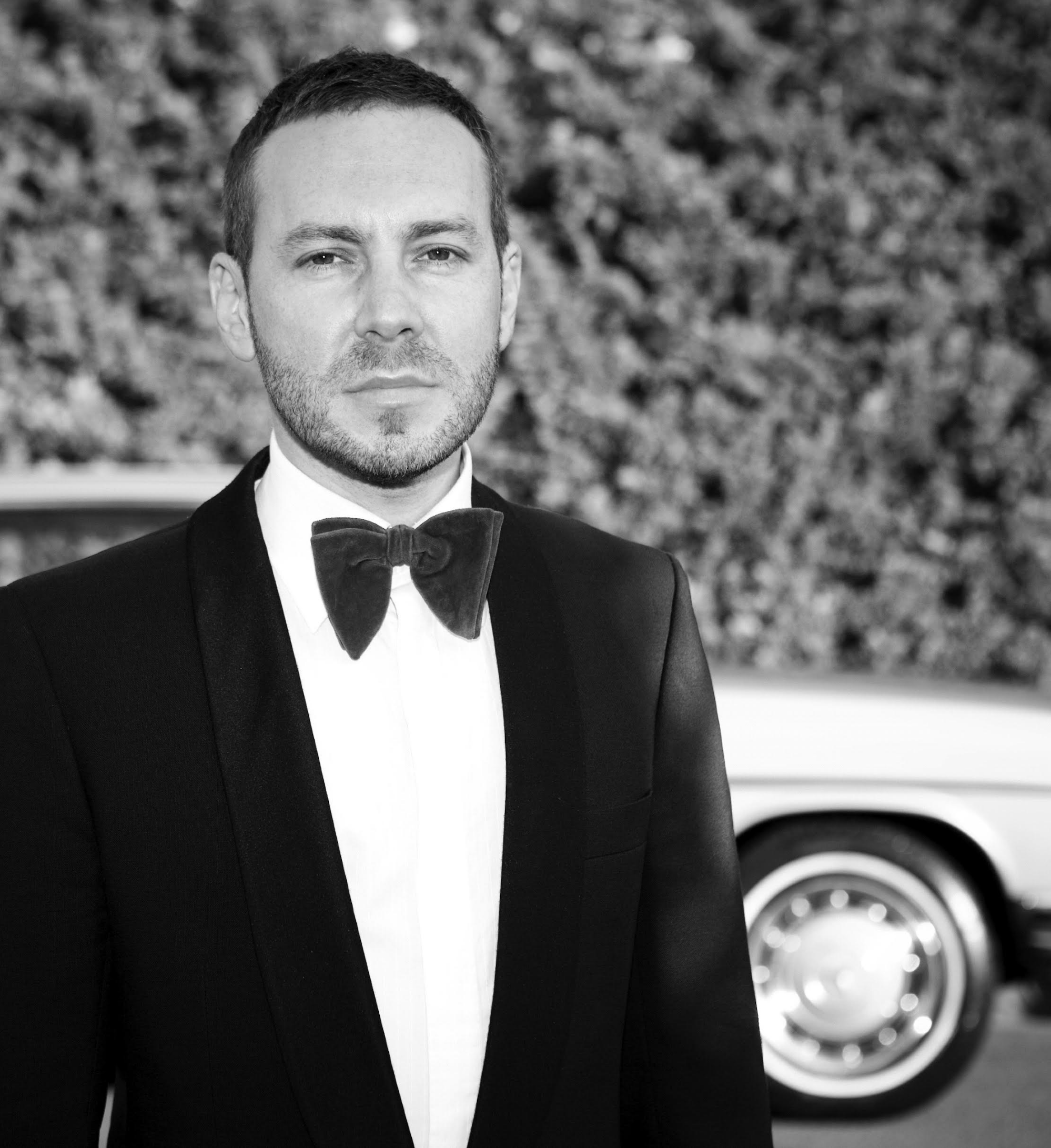 enter the workforce with cutting-edge knowledge and market-ready portfolios — prepared to add immediate value to employers or their own ventures.A man in formal tuxedo with bow tie standing outdoors near a classic car.