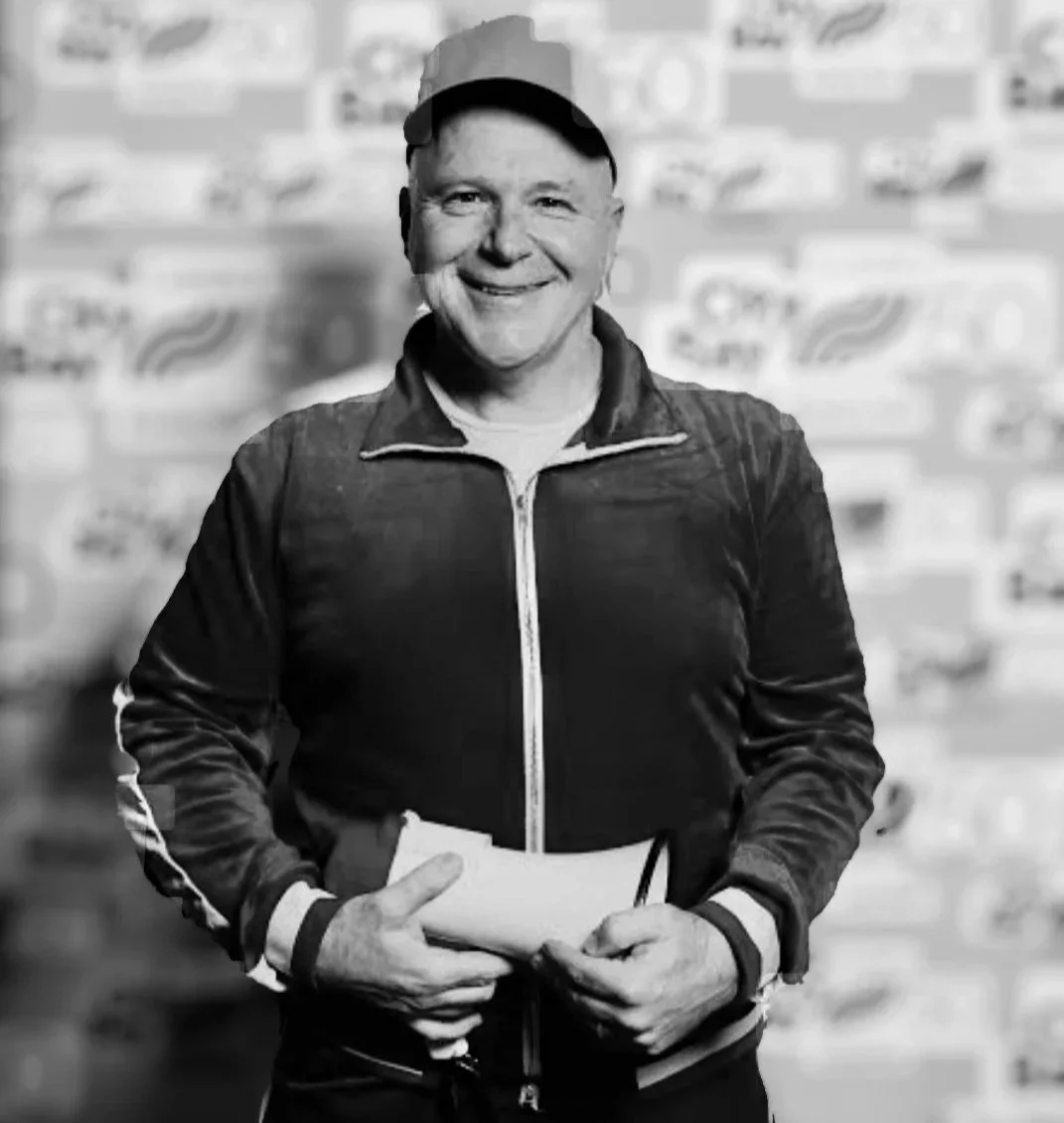 A smiling creative leader man in a jacket holding a notebook standing in front of a blurred background with various signs.