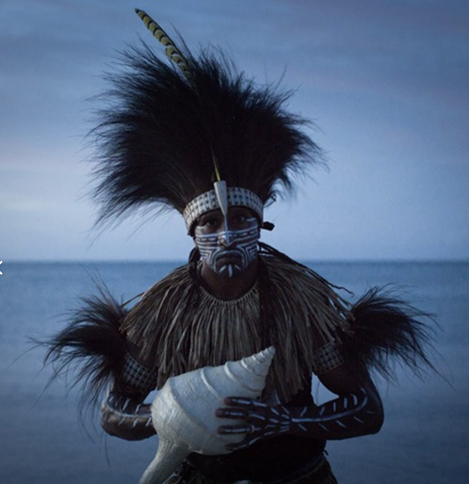 Explore TRIPLE AXEL - a revolutionary new platform designed to address talent retention, mentorship solutions and caIndigenous person wearing traditional attire and face paint, standing on a beach with the ocean in the background, holding a seashell.