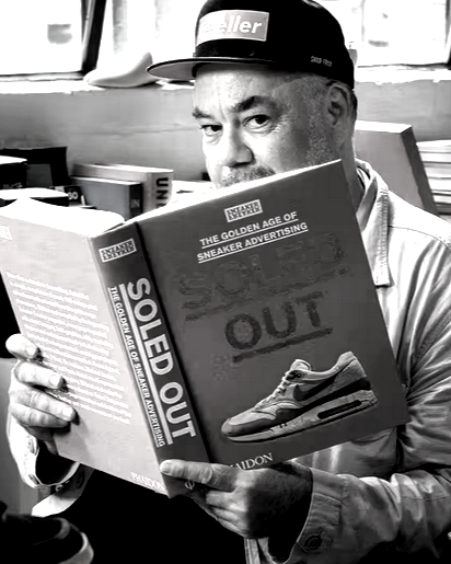 A man wearing a hat reading a magazine titled 'Sole Out' about sneaker advertising, with a picture of a sneaker on the cover.