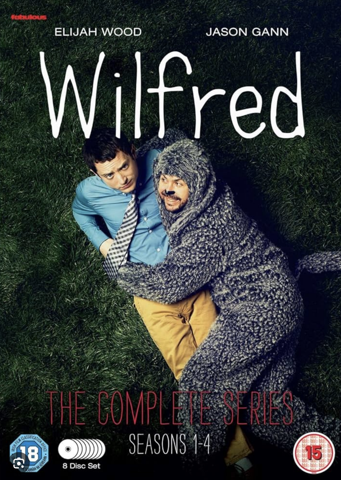 DVD cover for the TV series 'Wilfred' showing Elijah Wood and Jason Gann lying on grass, with Gann dressed as a dog and Wood in a shirt and tie, under the title 'Wilfred'.