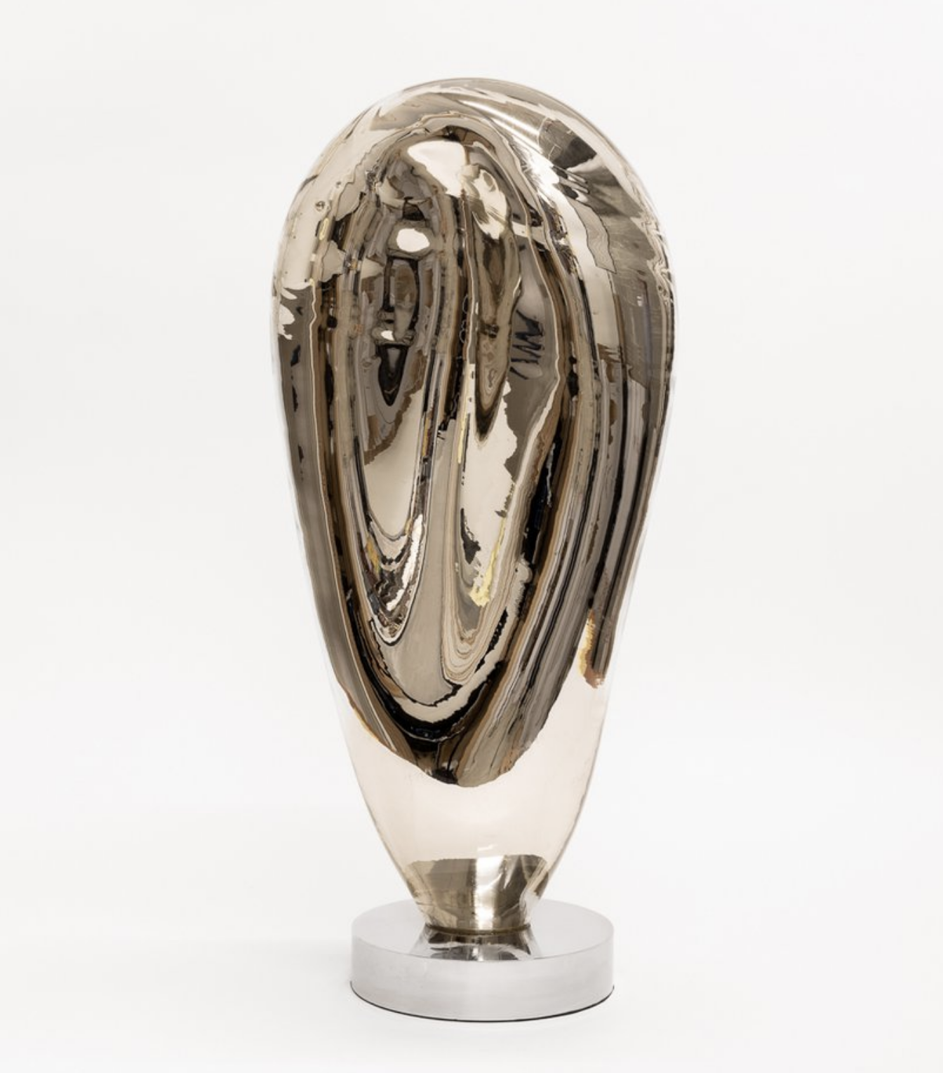A modern art sculpture made of reflective metallic material with an abstract, elongated shape, mounted on a circular base.