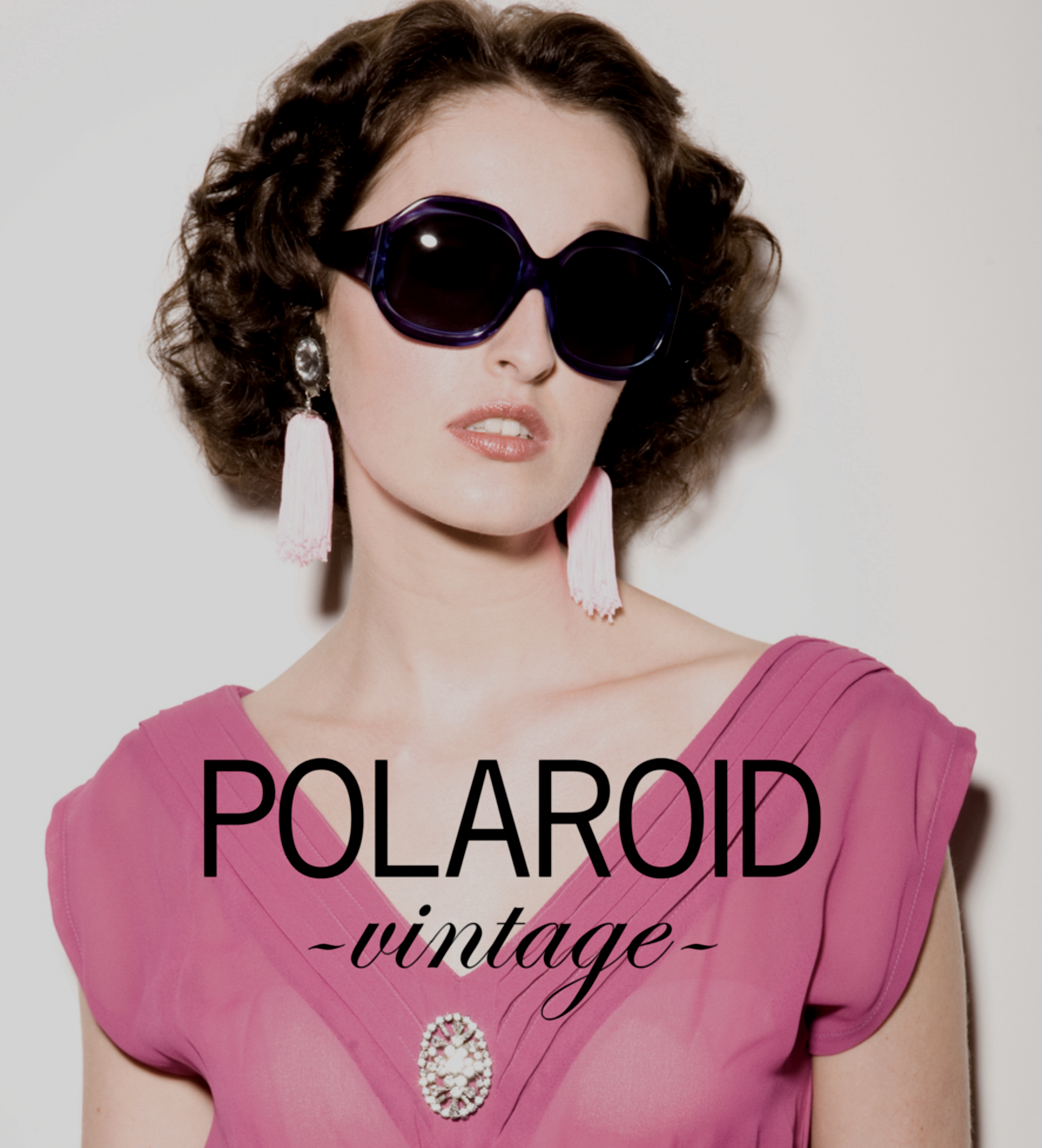 Woman wearing vintage pink dress with statement jewelry and large black sunglasses, background plain, text overlay says "POLAROID vintage".