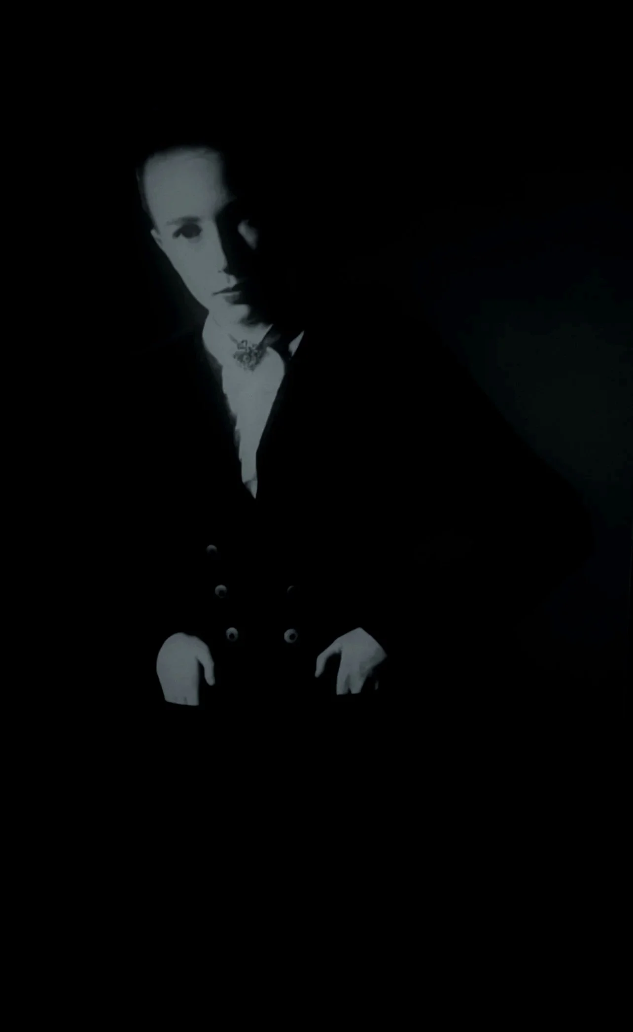 A black and white photo of a woman with short hair, dressed in vintage clothing, looking directly at the camera with a serious expression.