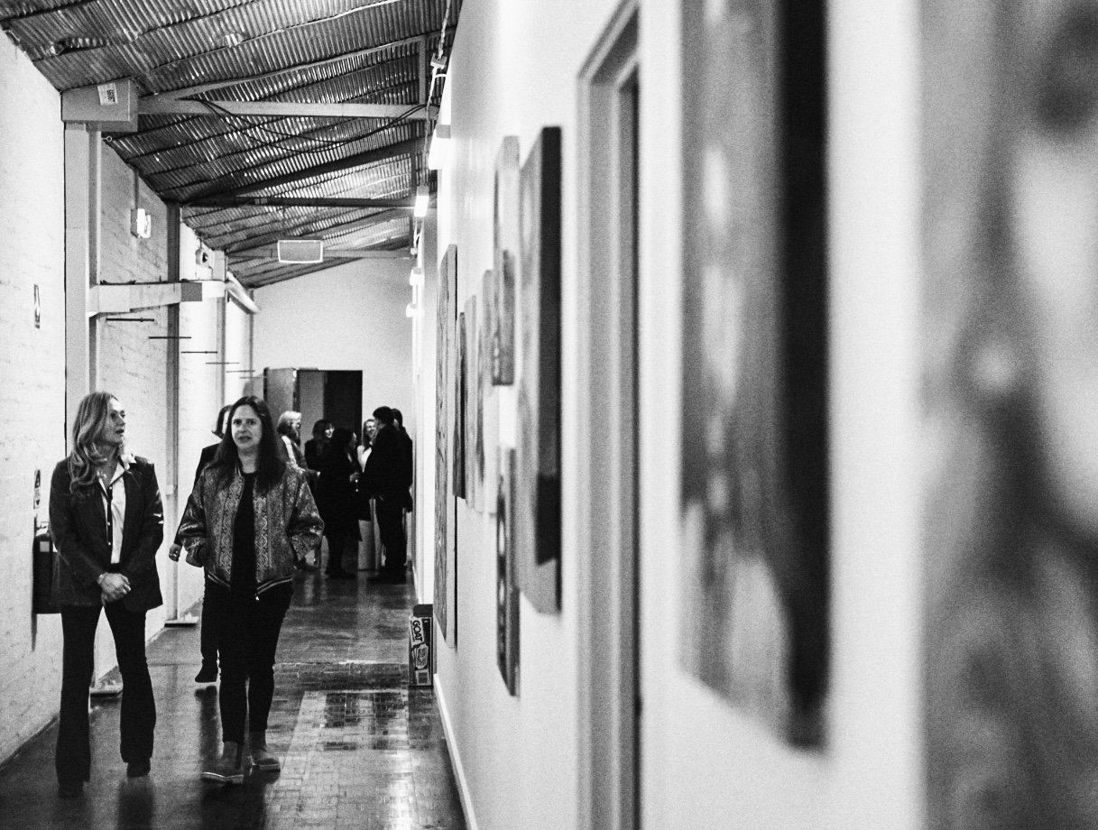 People walking through an art gallery with framed artwork on the walls in black and white.