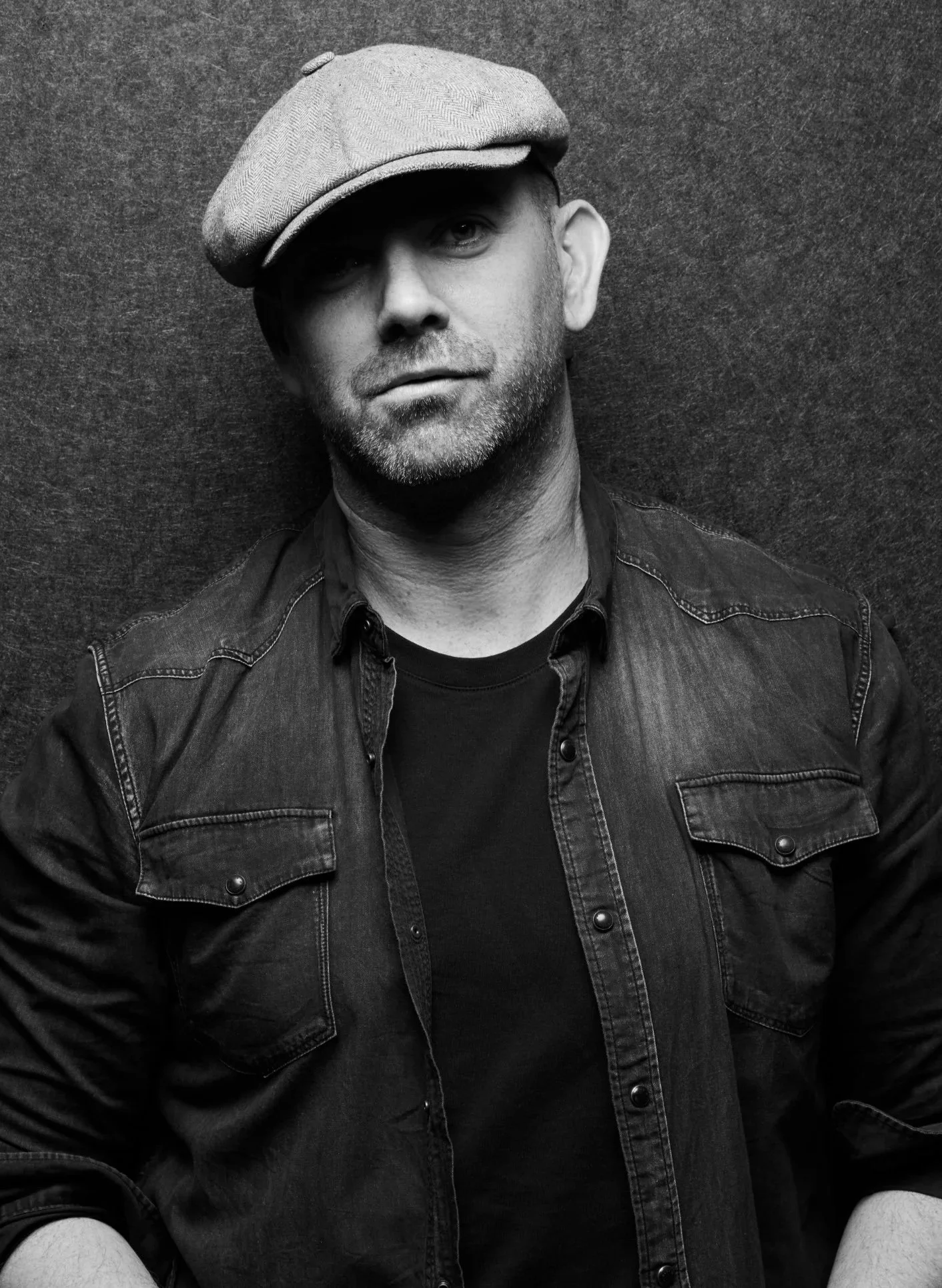 Explore TRIPLE AXEL - a revolutionary new platform designed to address talent retention, mentorship solutions and career resources. ABlack-and-white portrait of a man wearing a flat cap, denim jacket, and dark shirt, standing against a textured wall.