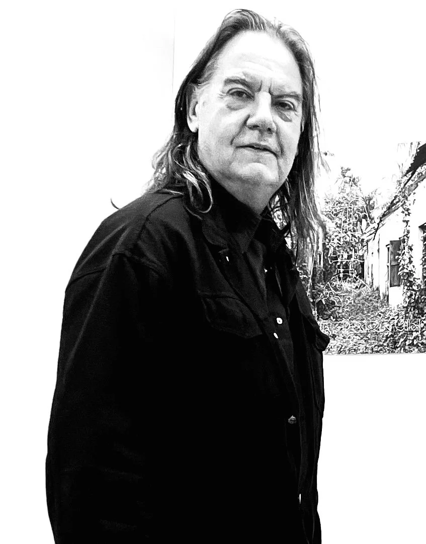 Black and white photo of a man with long hair wearing a black jacket, standing indoors with a botanical artwork on the wall behind him.