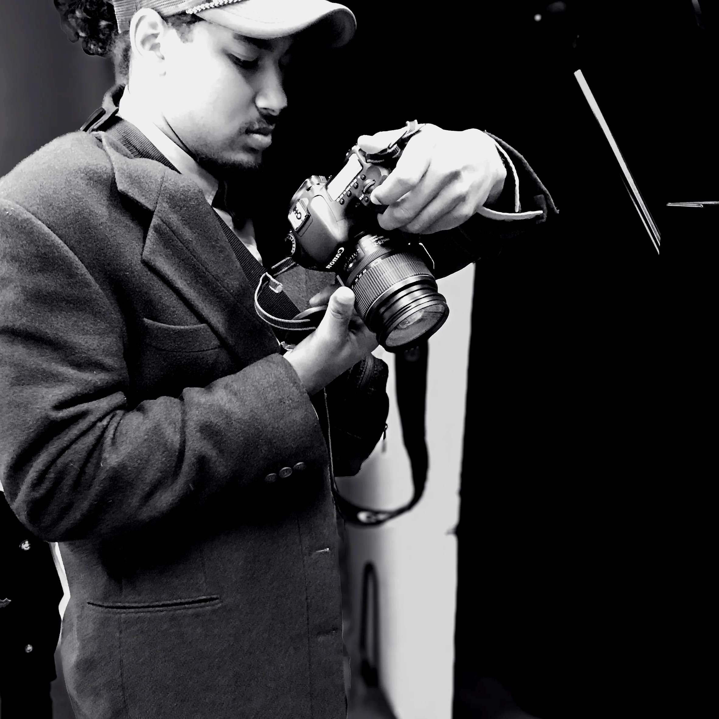 A man in a jacket and cap looking at a DSLR camera.