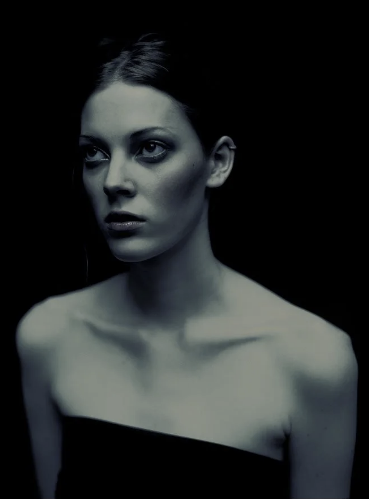 Black and white portrait of a woman with short hair, bare shoulders, and an intense expression, against a dark background.