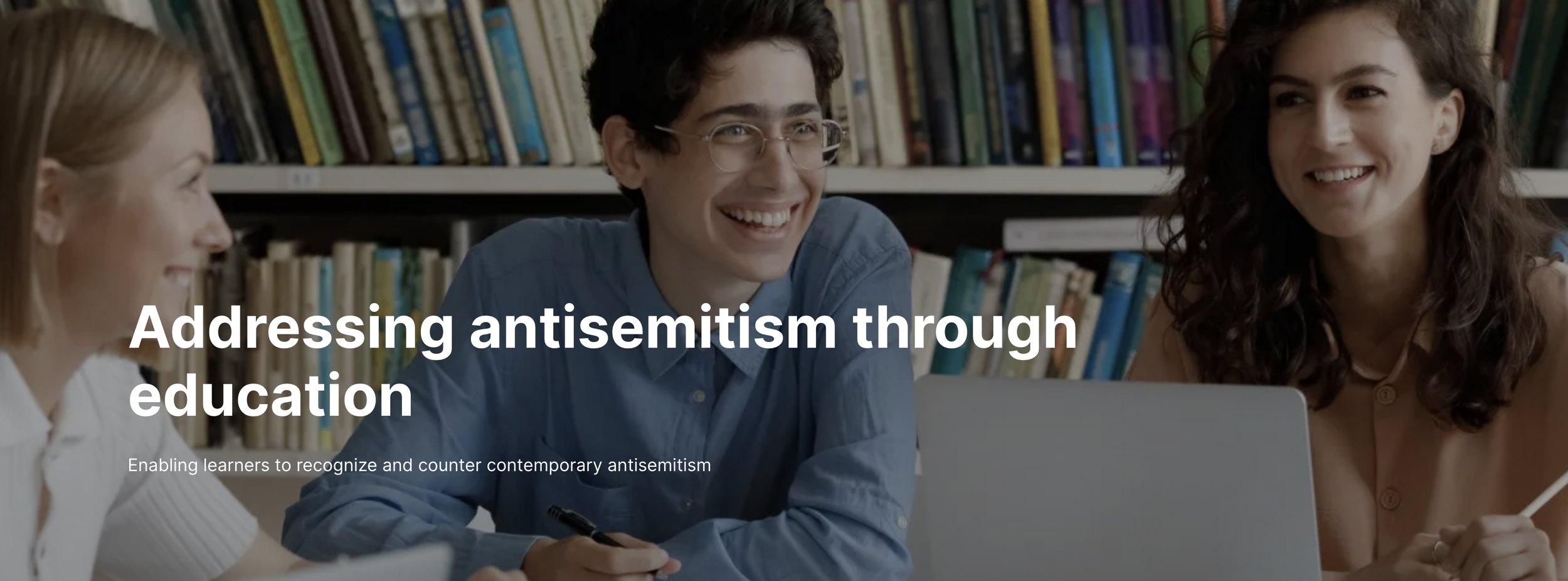 Three students in a library studying together, with bookshelves in the background, and the text 'Addressing antisemitism through education' overlaid.