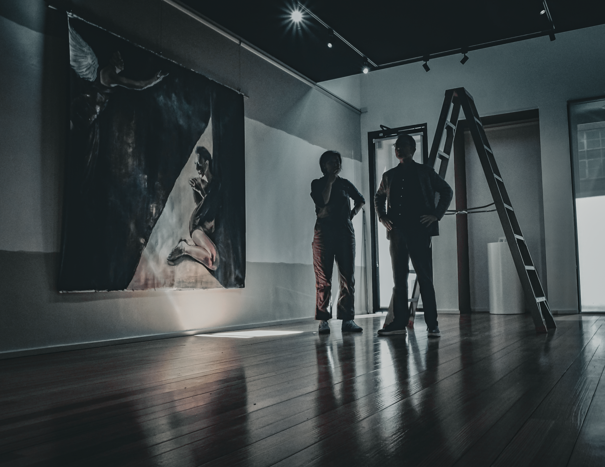 People standing inside an art gallery, looking at a large painting of a woman, with a ladder nearby, and a window in the background.