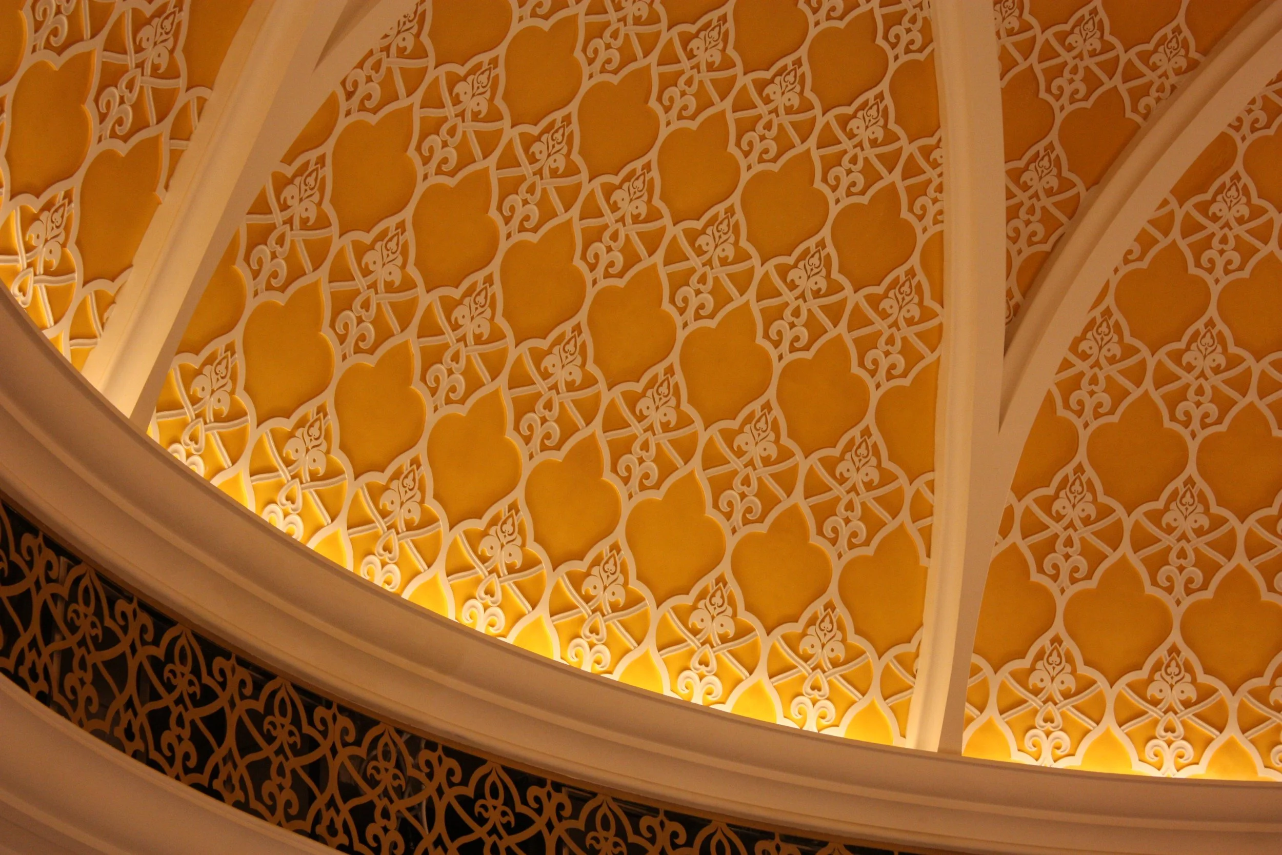 Détail d'un plafond décoratif orné de motifs géométriques et floraux dans des tons dorés et blancs.