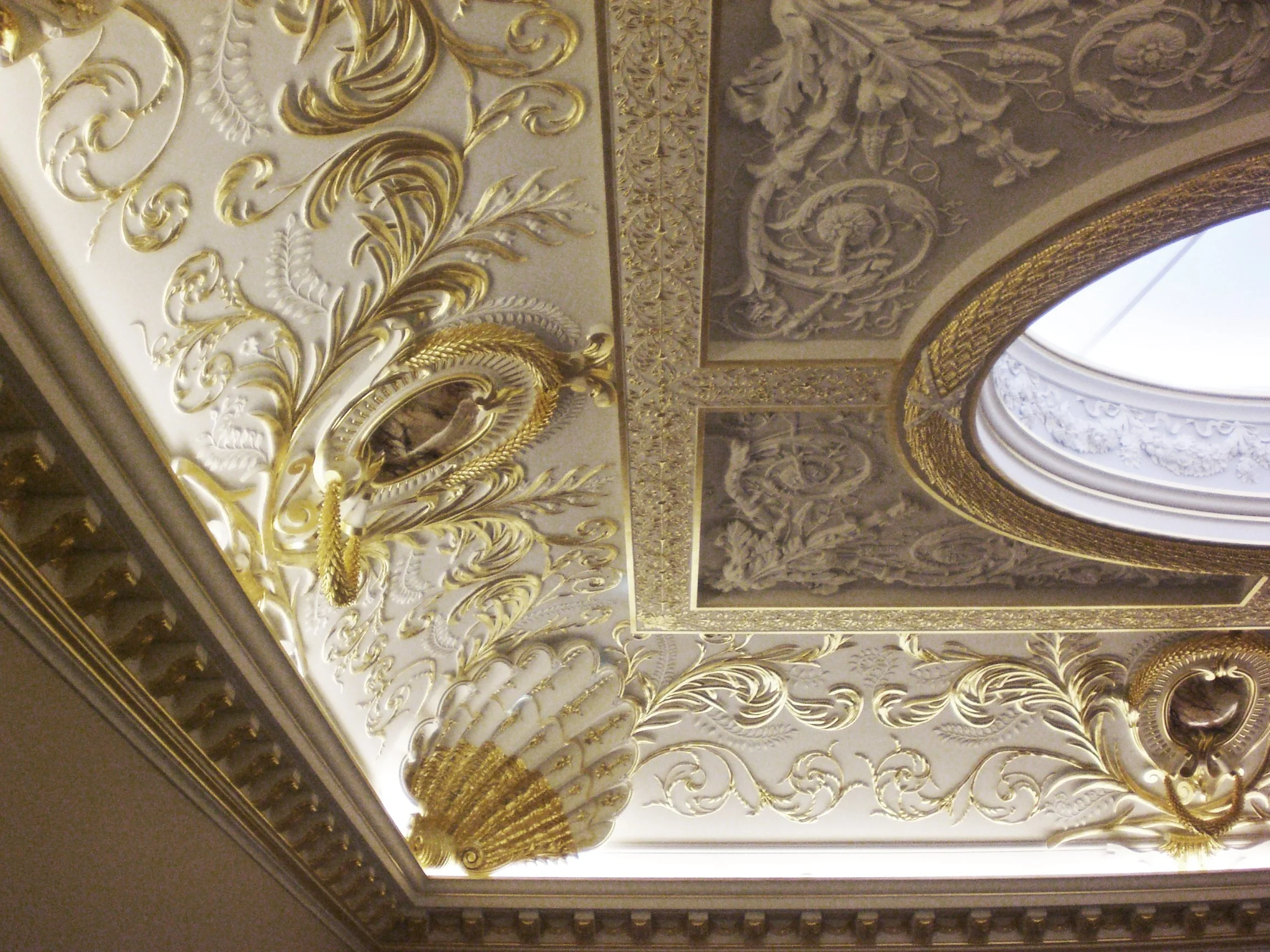Plafond orné de sculptures et de dorures avec un oculus lumineux.