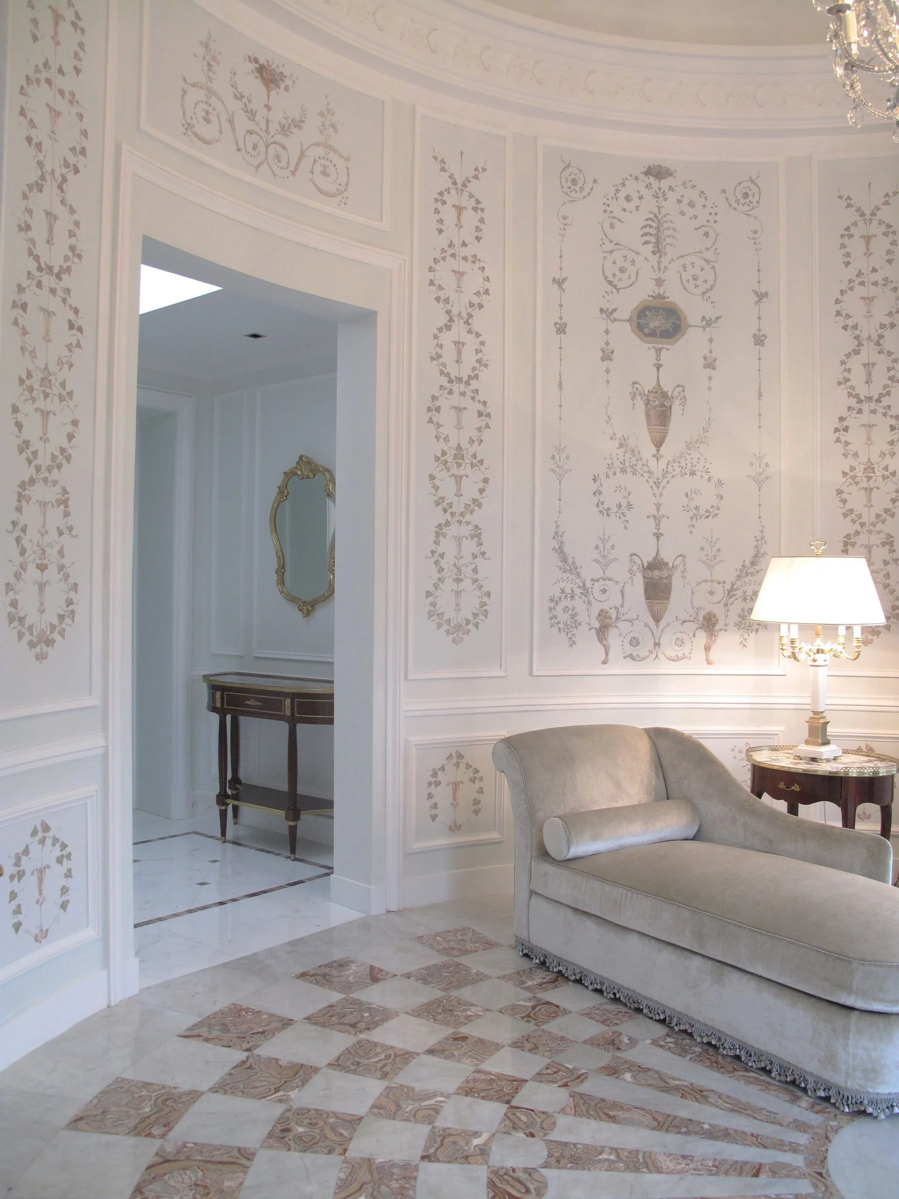 Intérieur d'une pièce élégante avec murs ornés de motifs or et blanc, canapé en velours beige, lampe de table et miroir doré